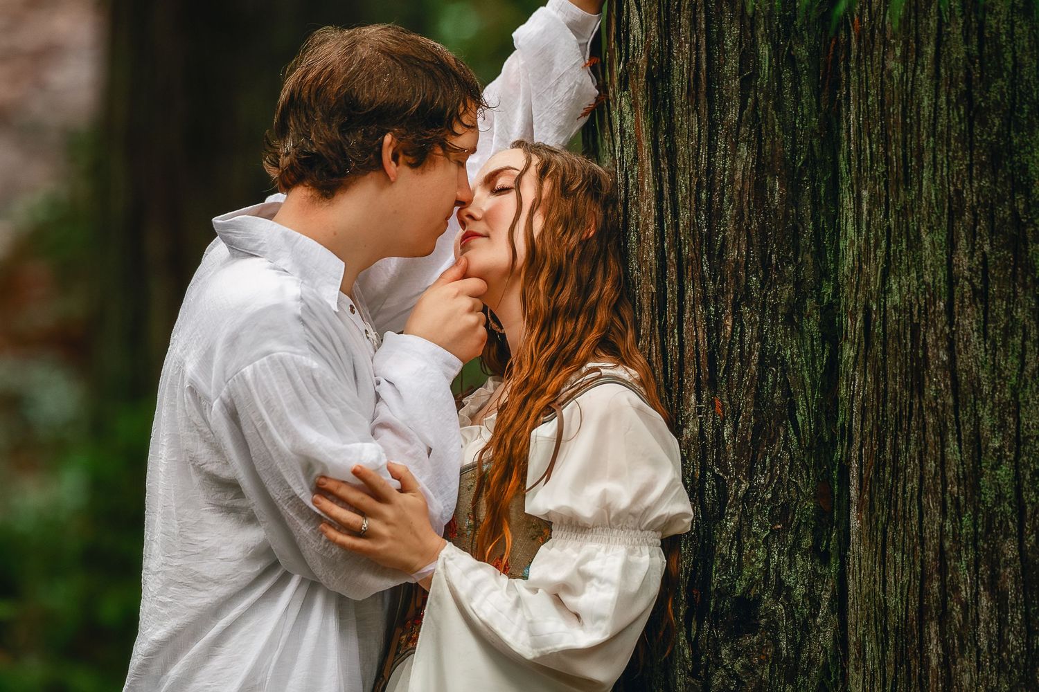 A couple in white outfits share romantic moments against a backdrop of tall trees in a forest setting.