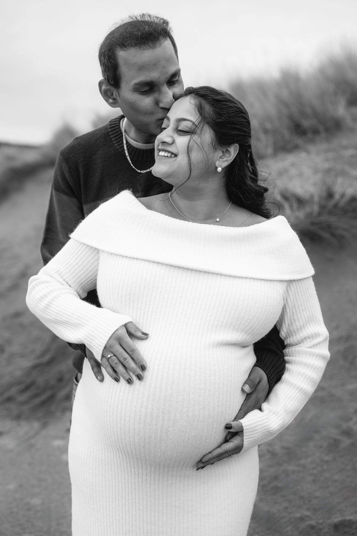 Black and white maternity photos showing couple embracing outdoors in romantic poses.