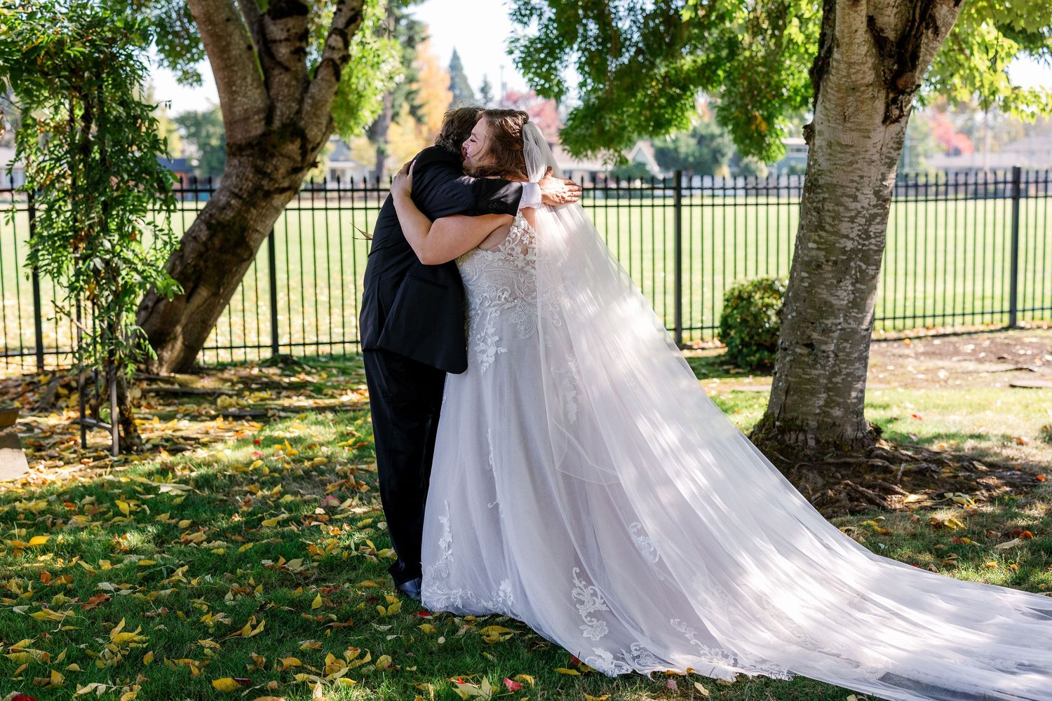 A couple shares a romantic moment under sunlit trees in a garden setting during their wedding celebration.