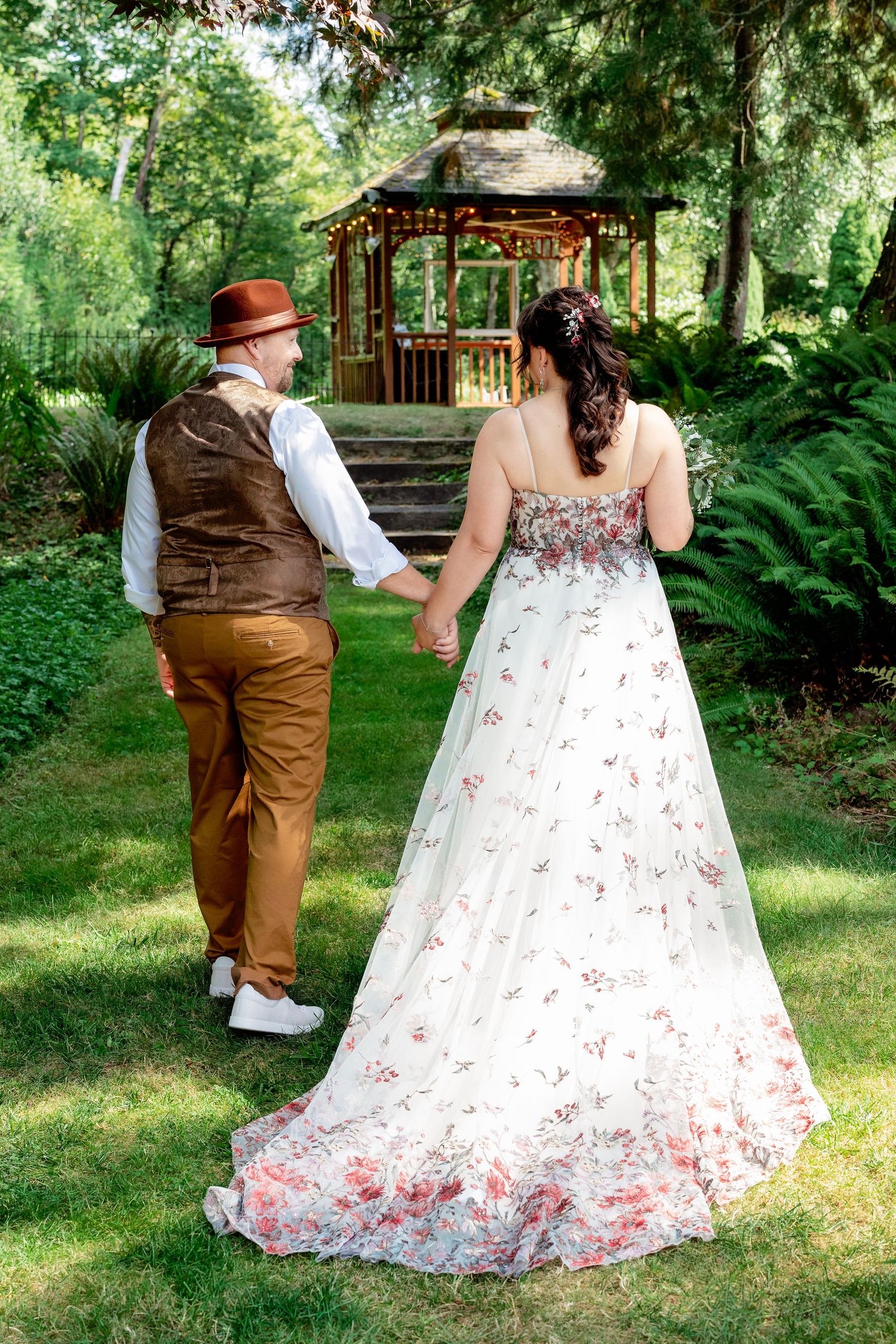 A couple in vintage-inspired wedding attire poses in a lush garden setting with ferns and greenery.