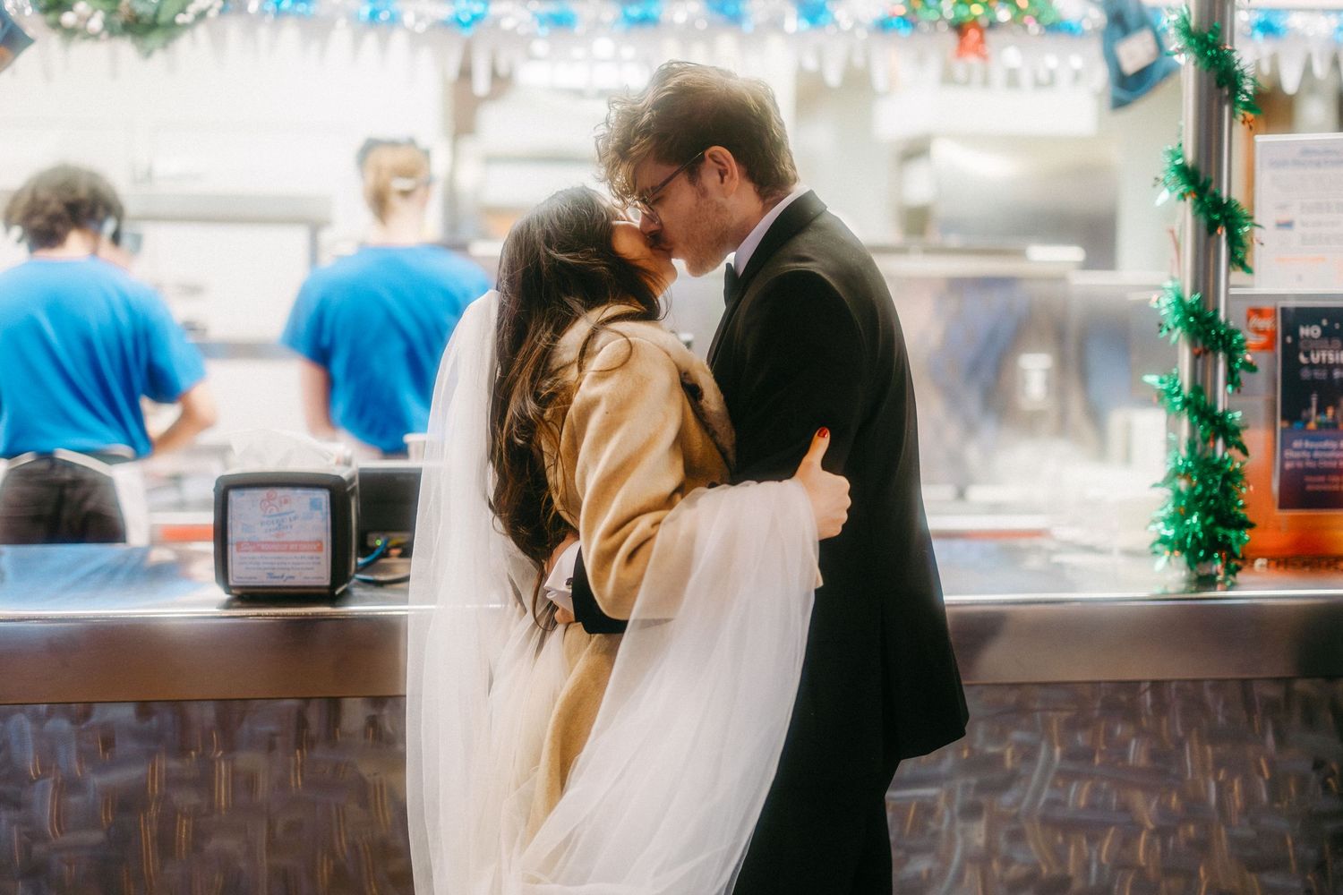 A couple embraces in front of a food counter while waiting in line at a casual restaurant.