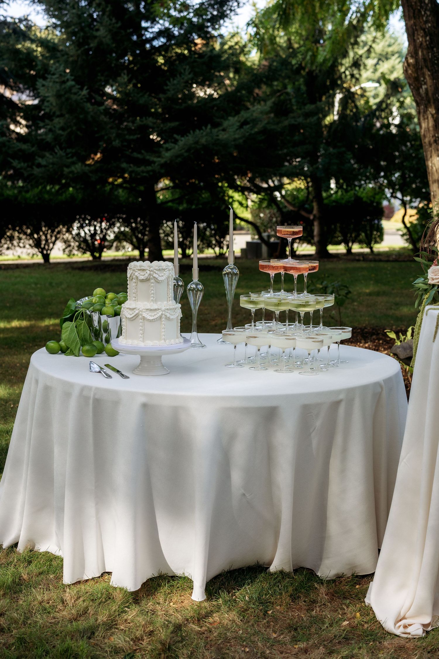 Elegant outdoor wedding reception setup with white-clothed tables against a backdrop of trees.