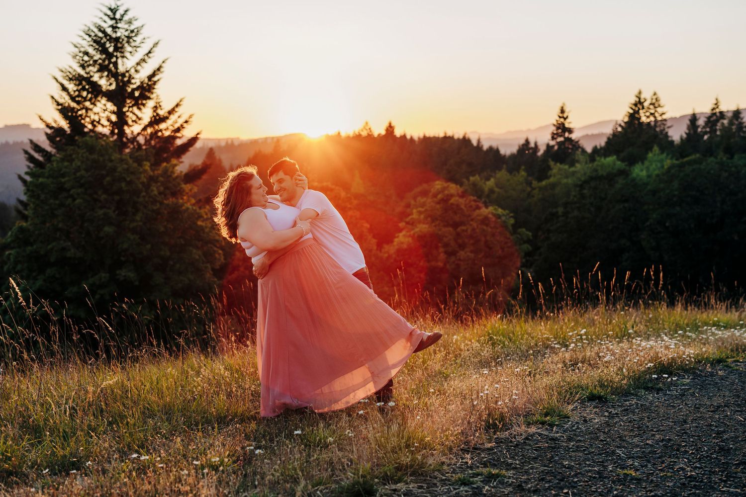 Silhouettes of evergreen trees against a vibrant orange sunset sky create a peaceful mountain landscape.