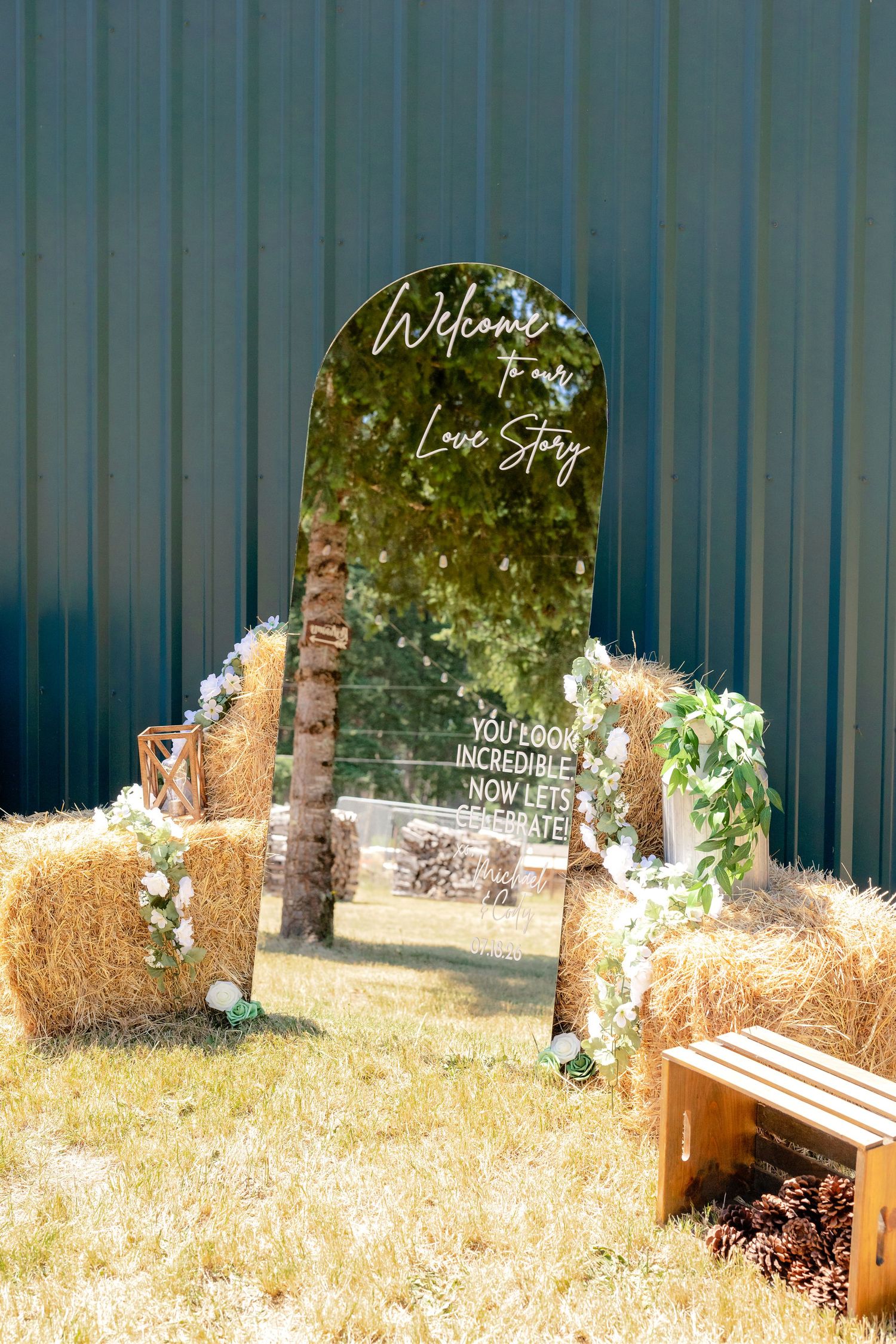 A decorative wedding welcome mirror sign reading Welcome to Our Love Story displayed on hay bales outdoors.