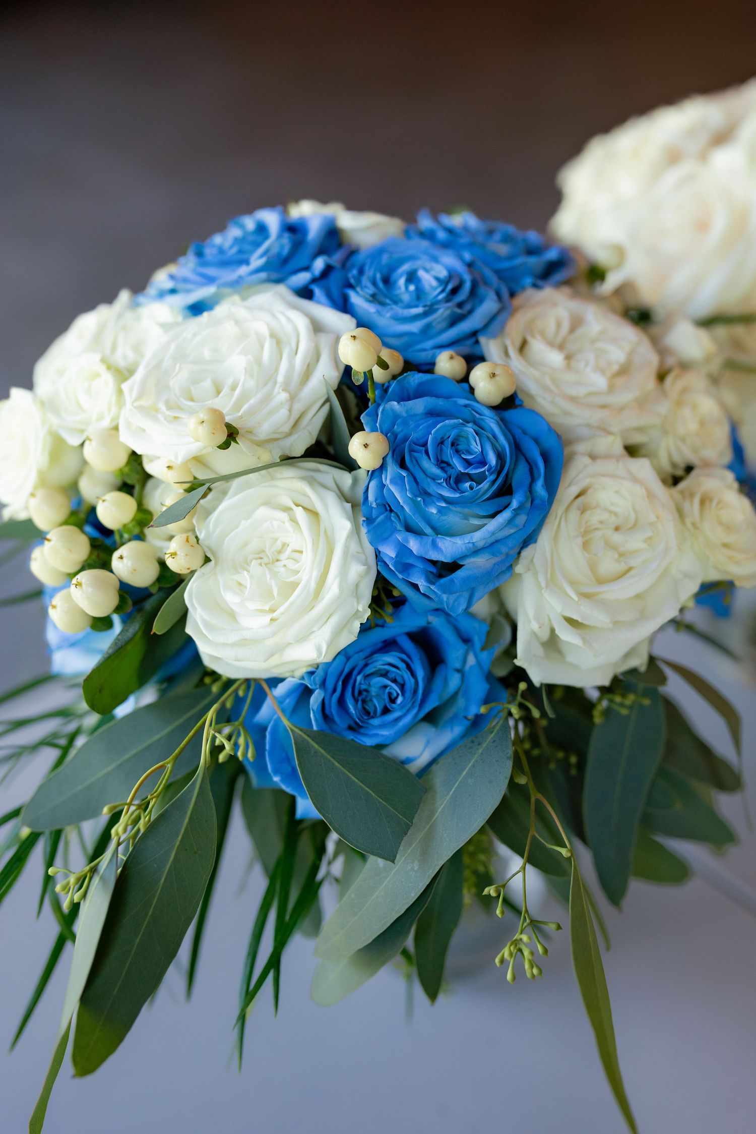 Elegant bridal bouquet featuring blue and white roses with green eucalyptus leaves.