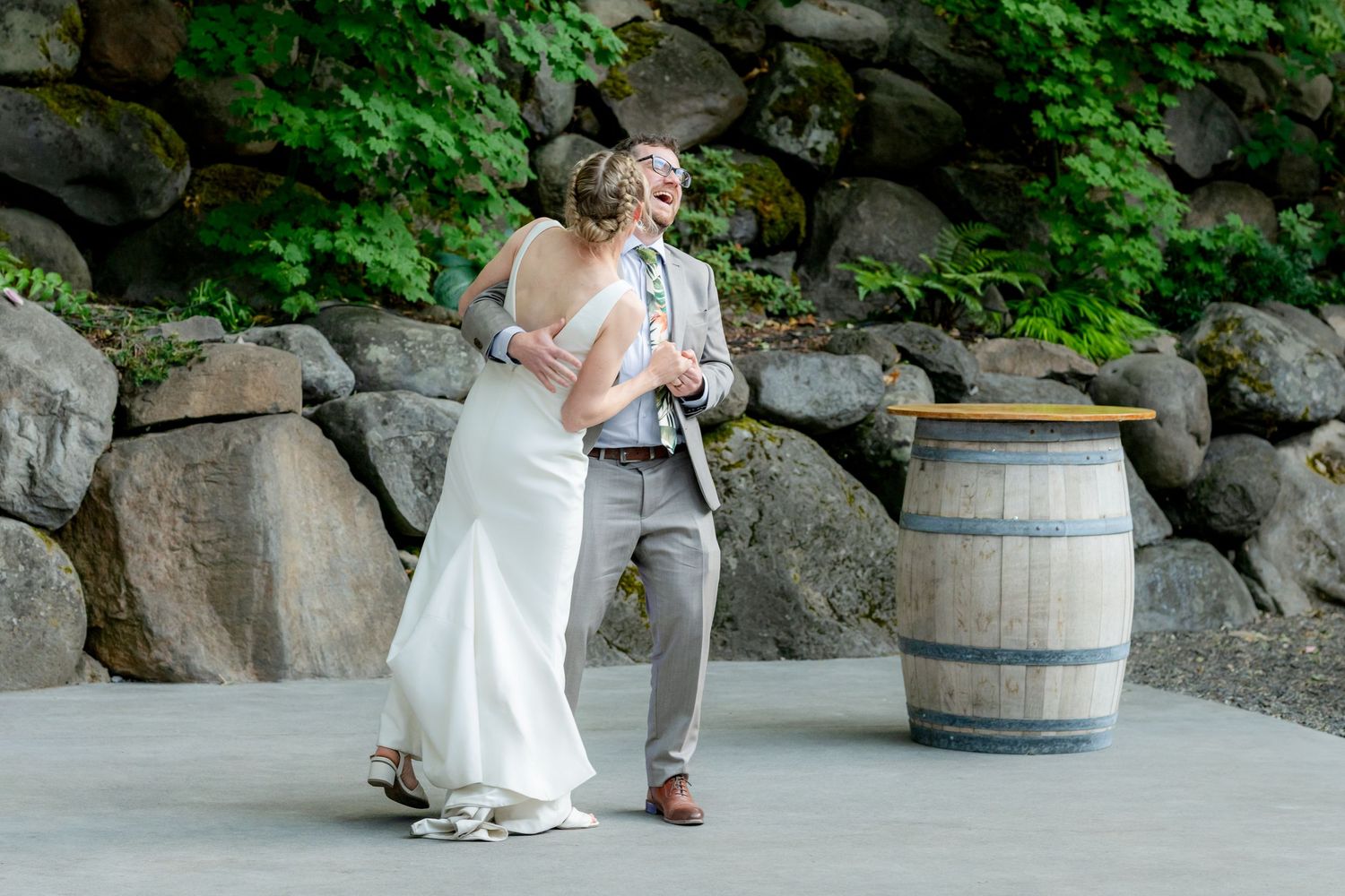 Bride and groom share a joyful first dance outdoors near a rustic wooden barrel at their wedding reception.
