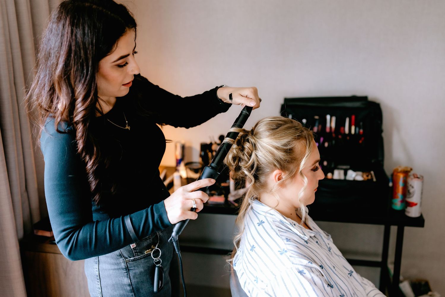 A hairstylist curling a blonde woman's hair in a modern salon setting.