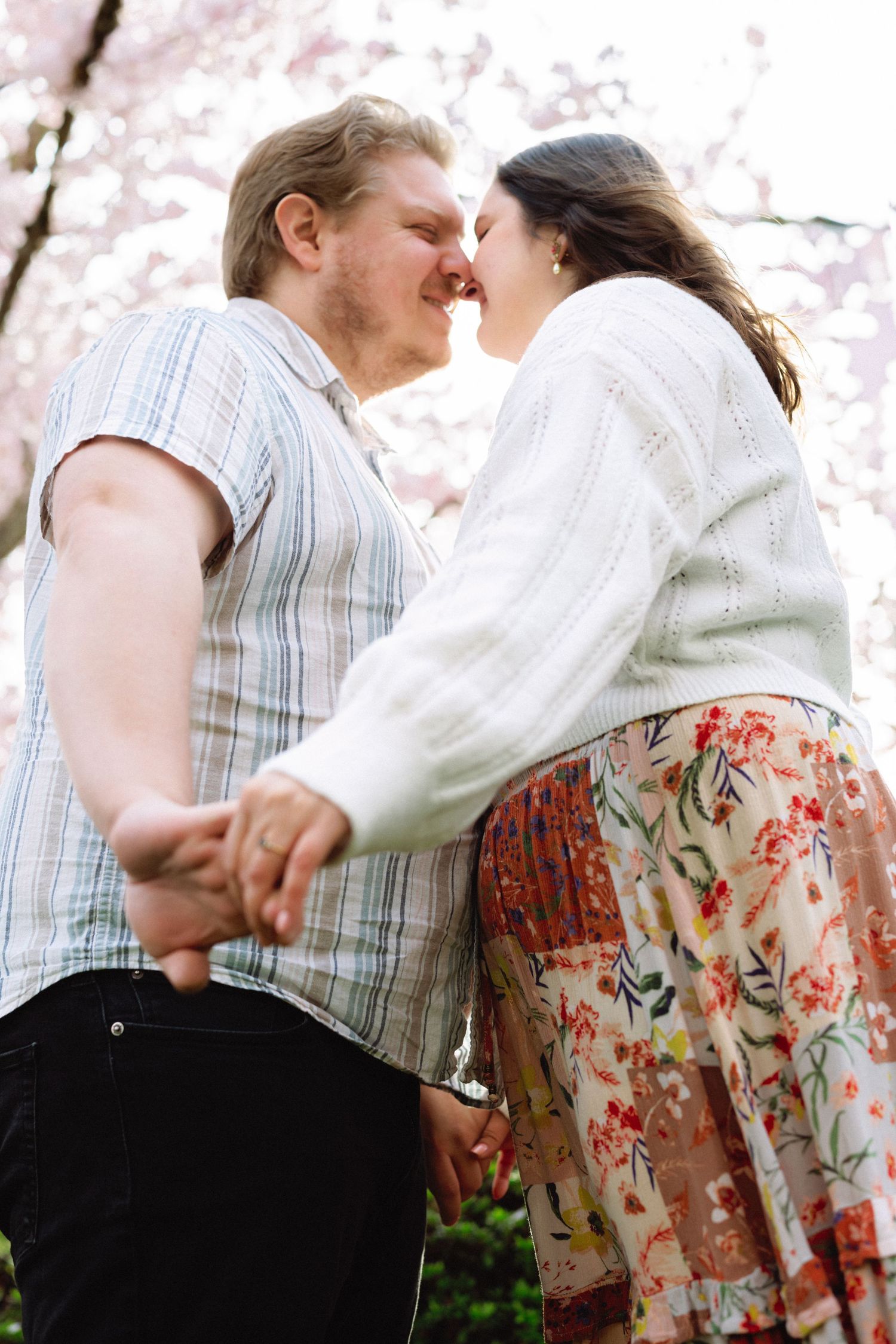 A couple shares an intimate moment outdoors with cherry blossoms blooming in the background.