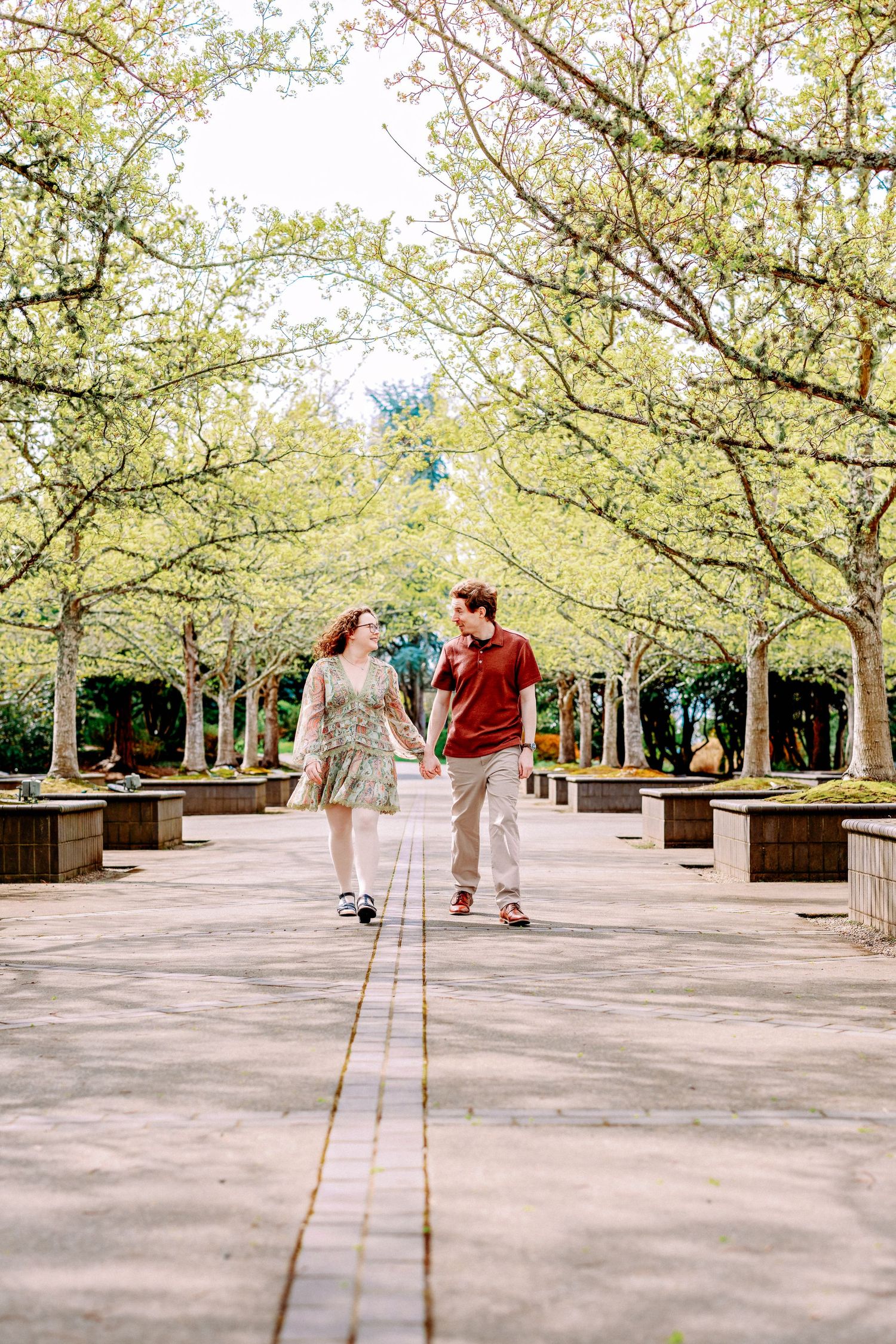 A couple walks hand in hand beneath blooming cherry blossom trees in a tranquil garden pathway.