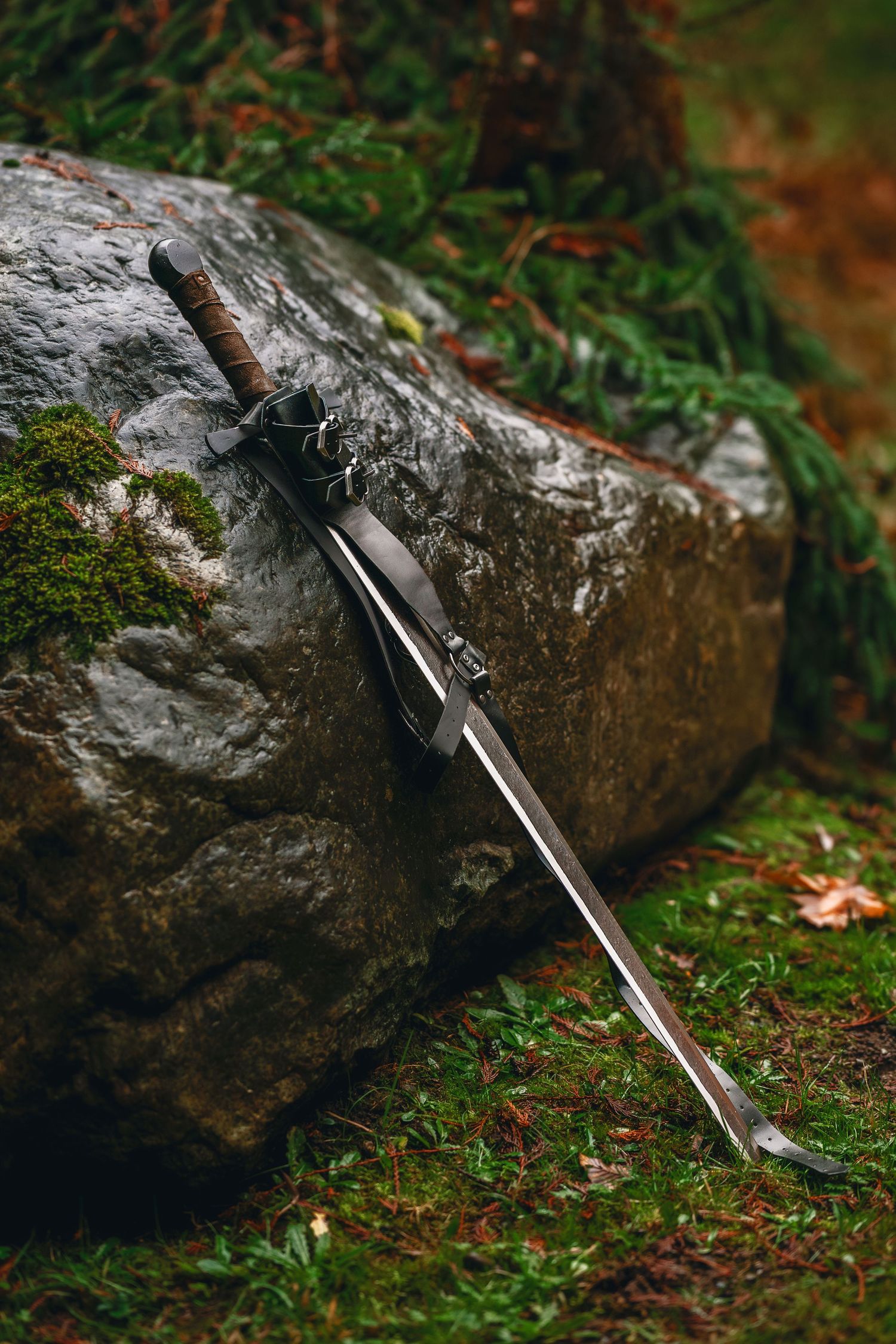 A silver sword lies on mossy ground next to large rocks in a forest setting.