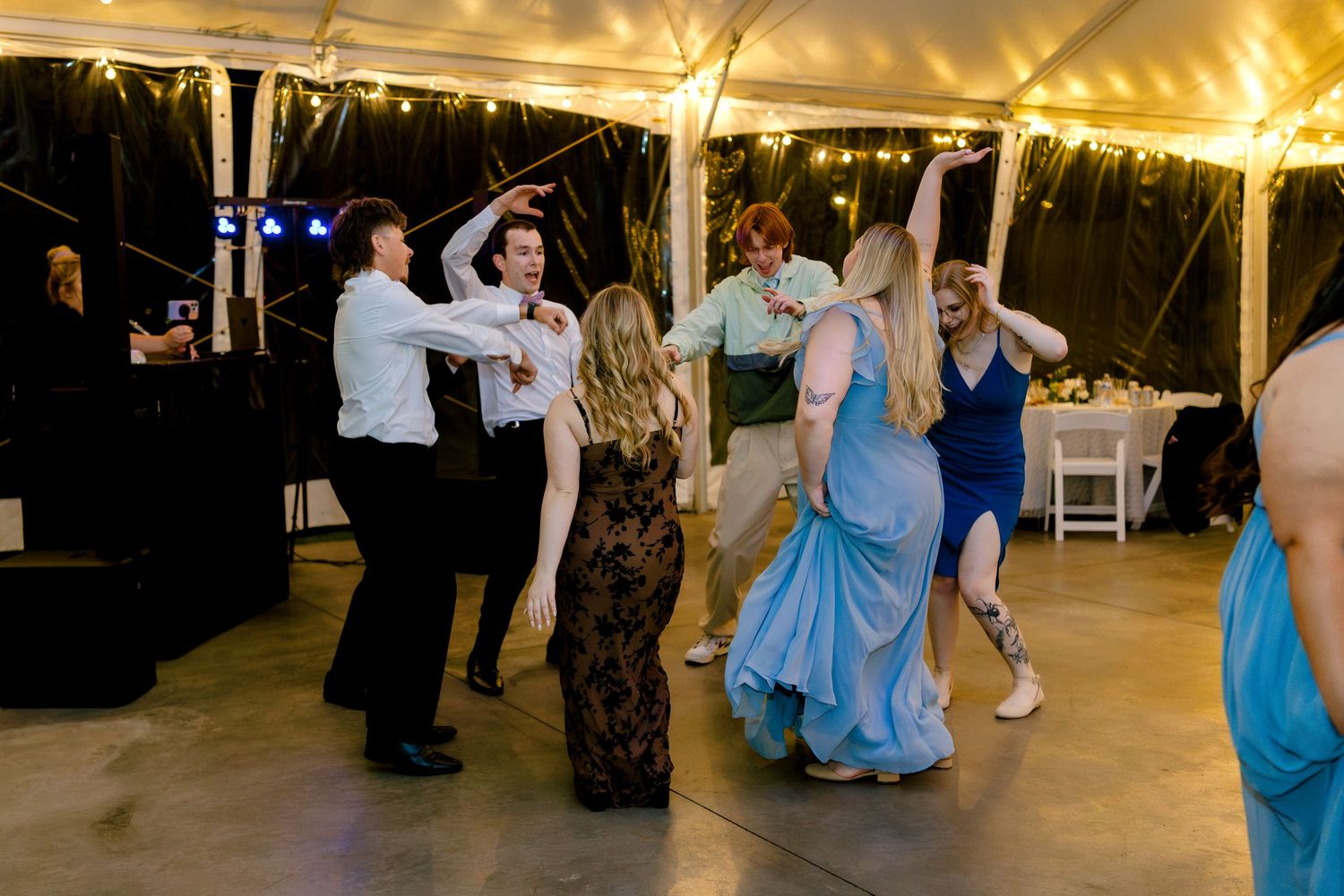 People dancing and celebrating under a white tent at an outdoor evening reception with string lights overhead.