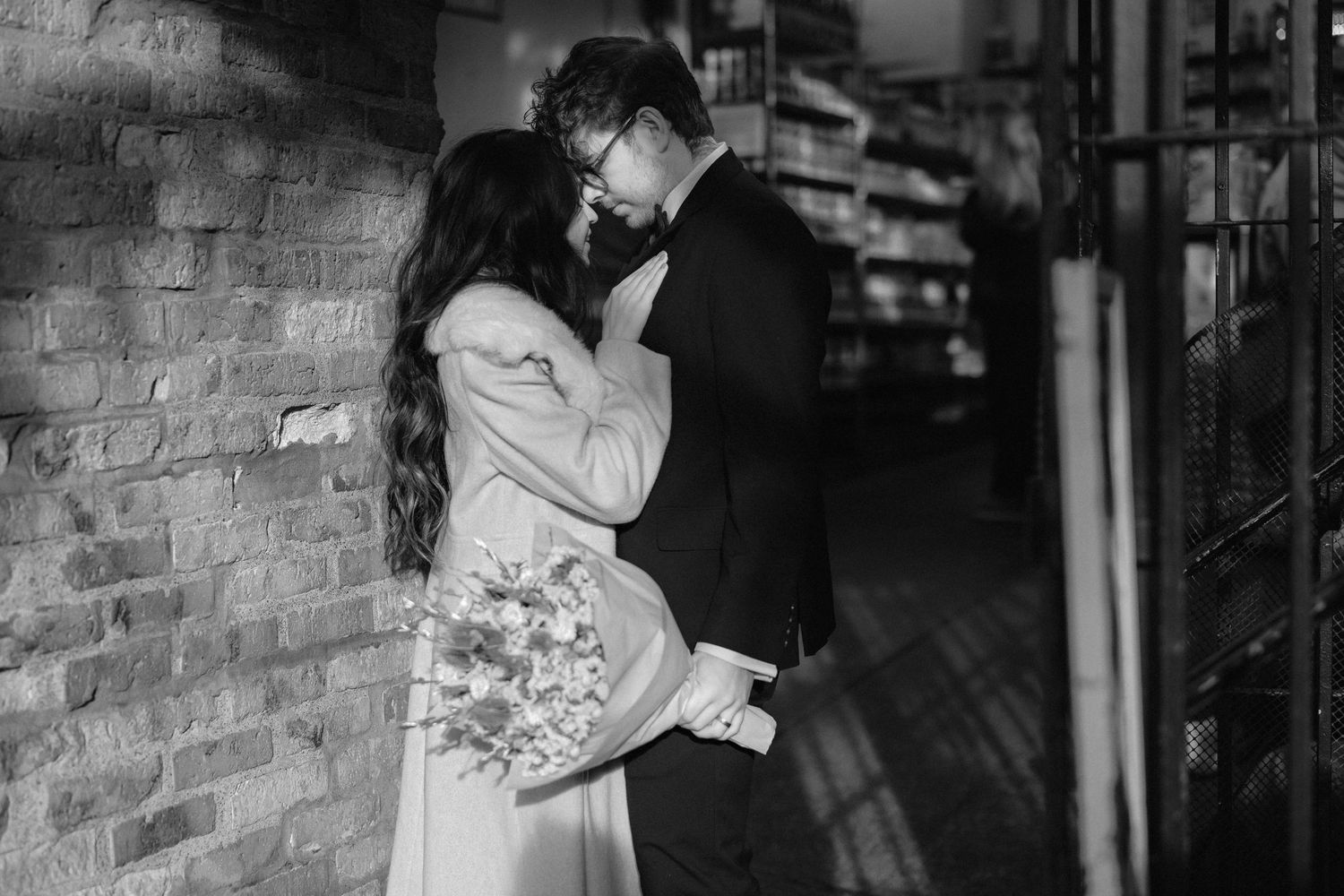 A romantic black and white photo of a couple dancing at their wedding reception in a brick-walled venue.