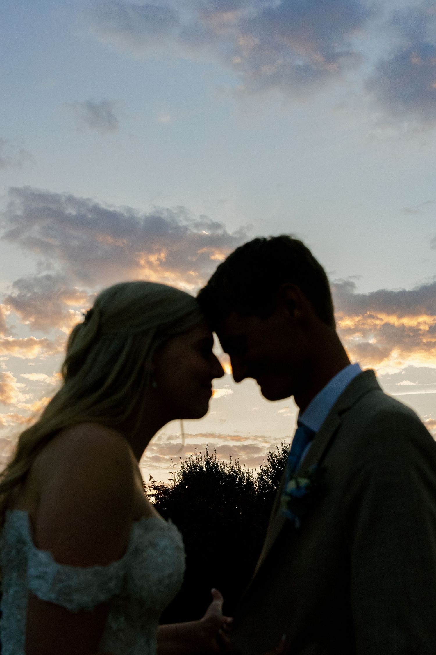 Silhouette of a couple sharing an intimate moment at sunset with colorful clouds in the background.