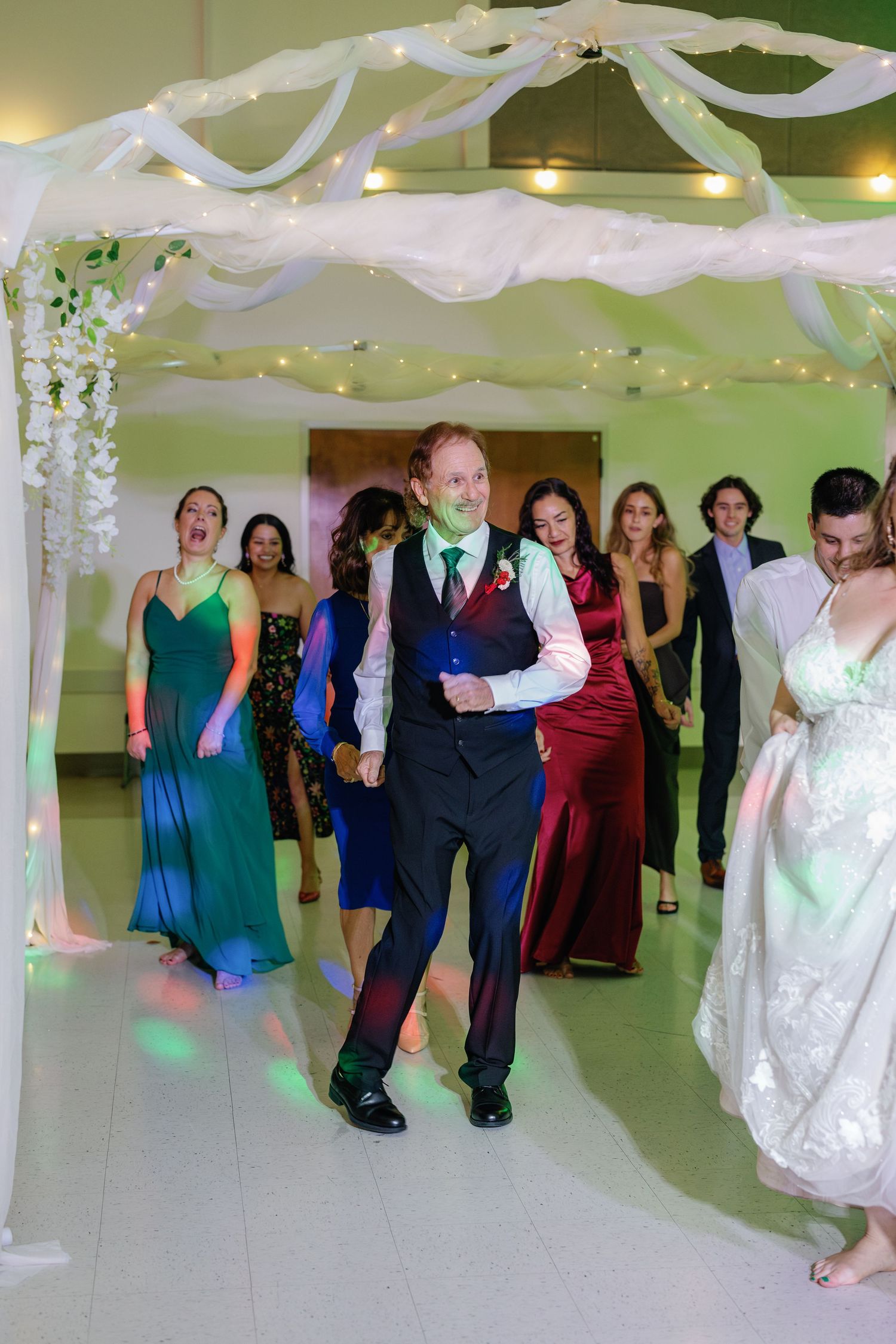Wedding guests dancing under white fabric decorations and string lights in a reception hall.
