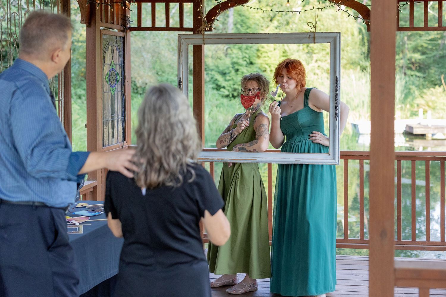 Wedding ceremony guests gathered in a wooden gazebo surrounded by green trees and natural light.