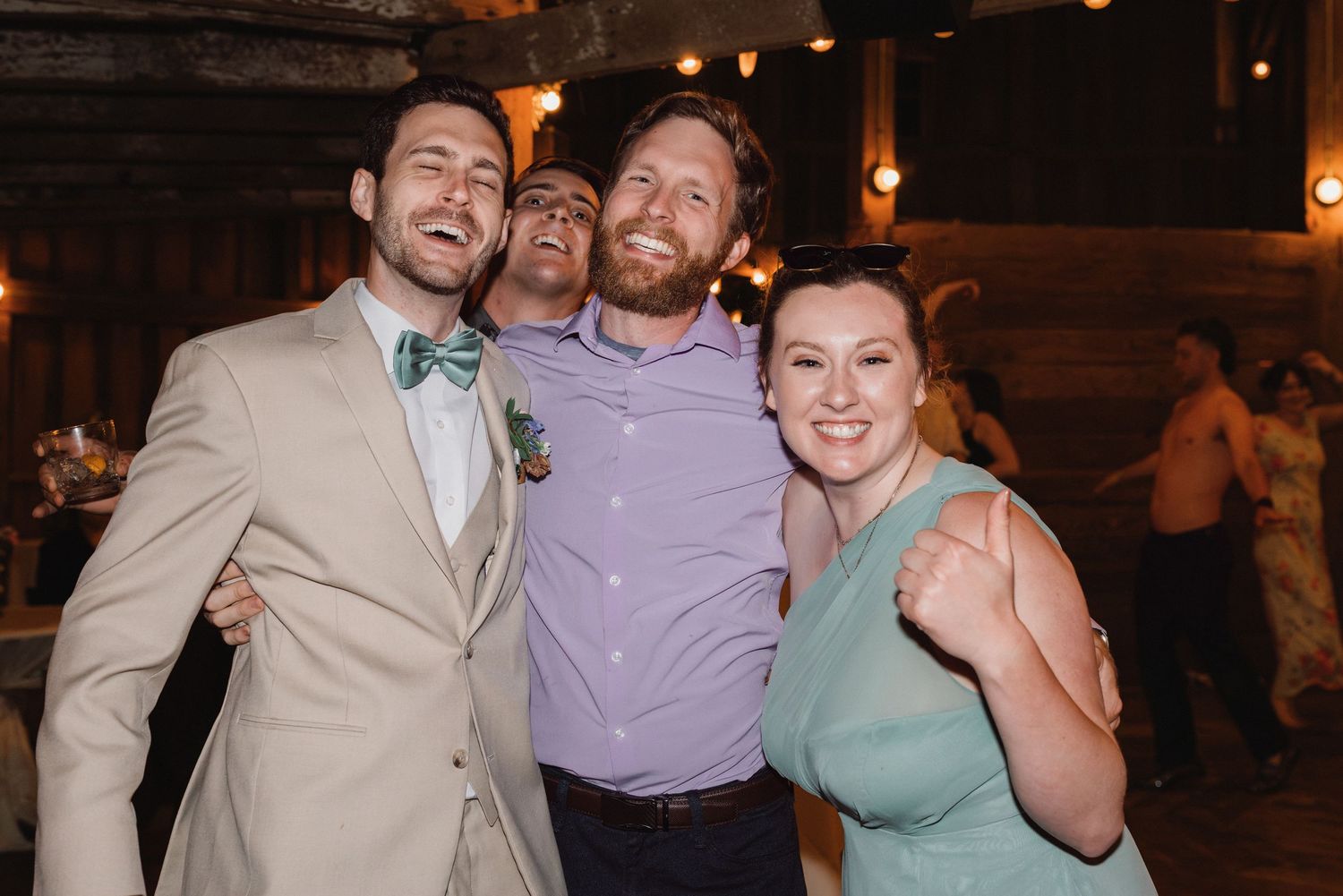 Four wedding guests smiling and posing together on dance floor at indoor wedding reception.