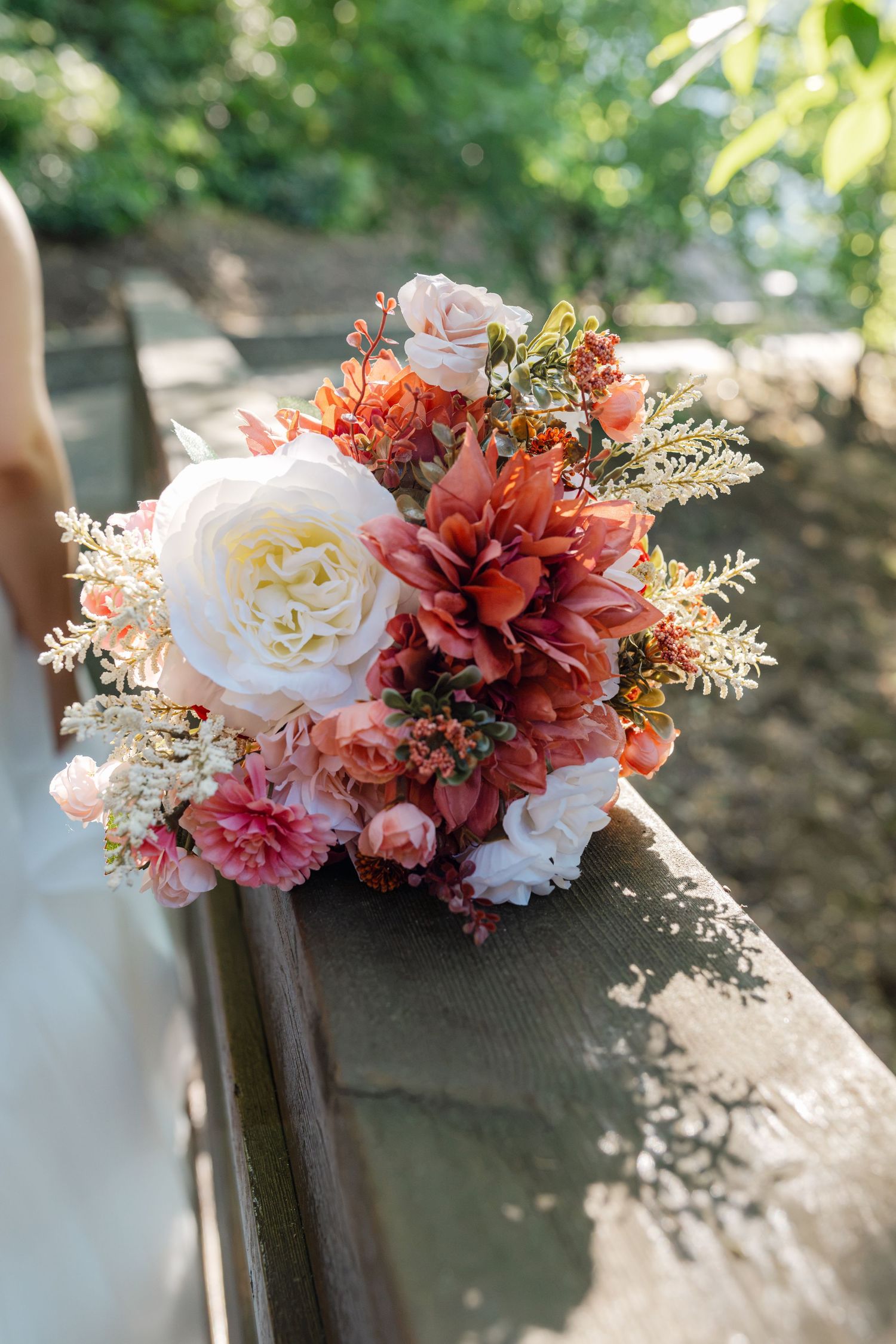 Bridal bouquet of coral, pink, and white flowers rests on wooden railing outdoors.