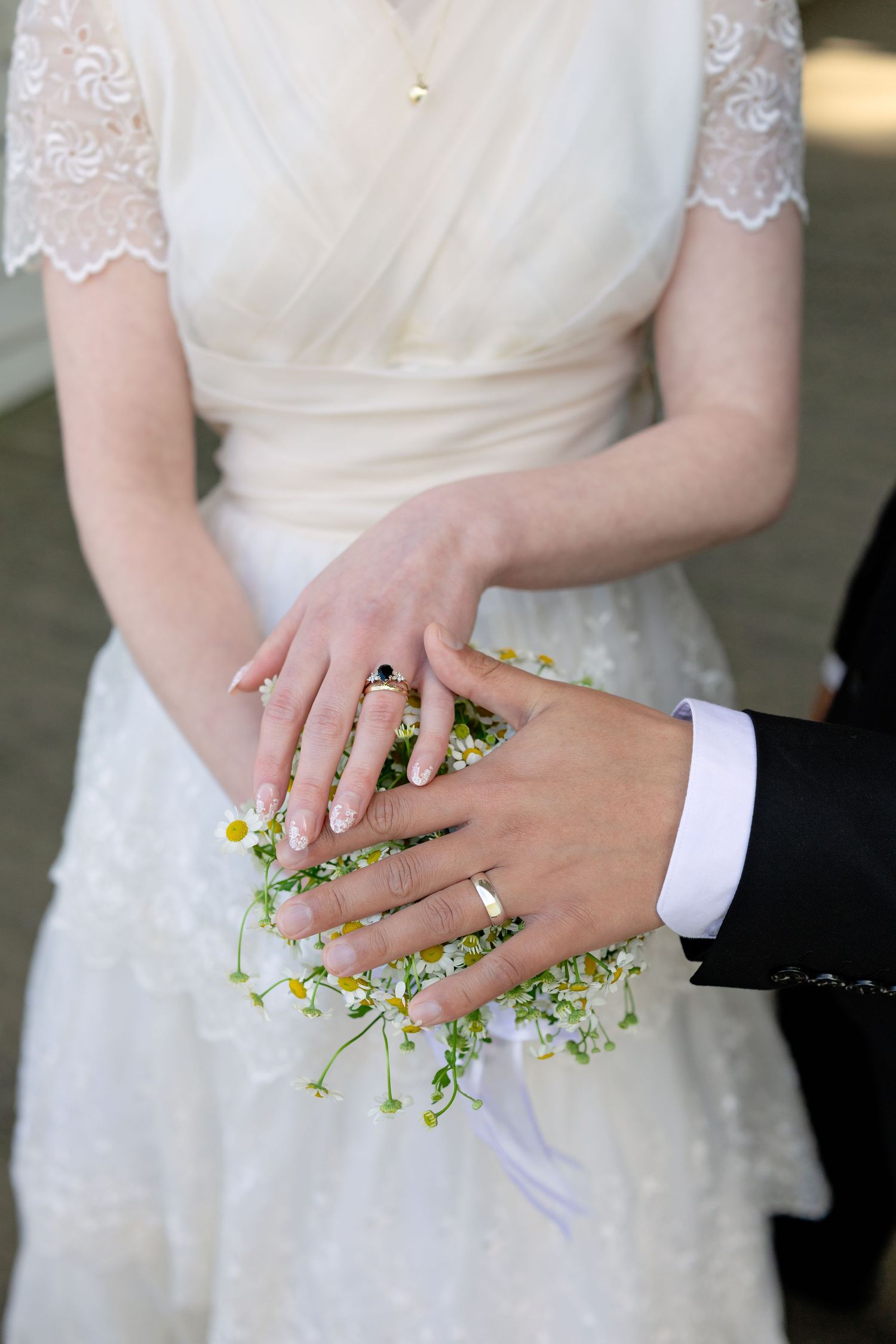 Newlyweds display wedding rings over a delicate wildflower bouquet in a lace wedding dress.