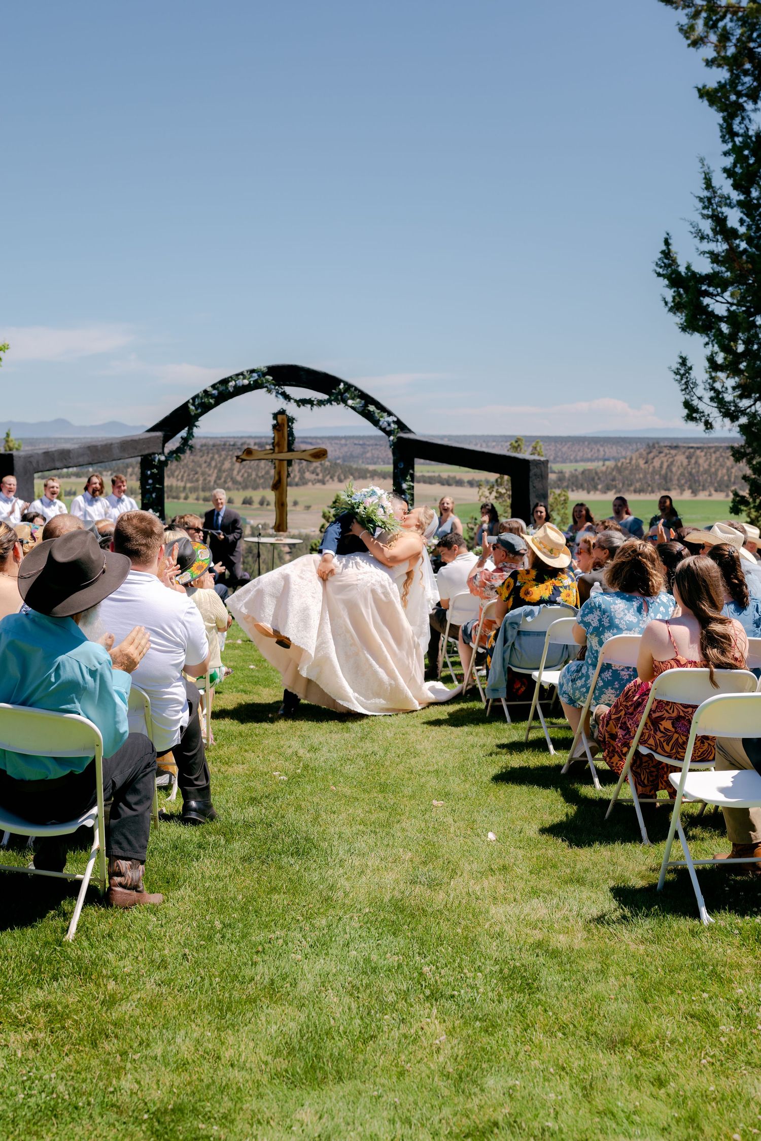 Bride walks down the aisle at an outdoor wedding ceremony on a sunny day with mountain views.