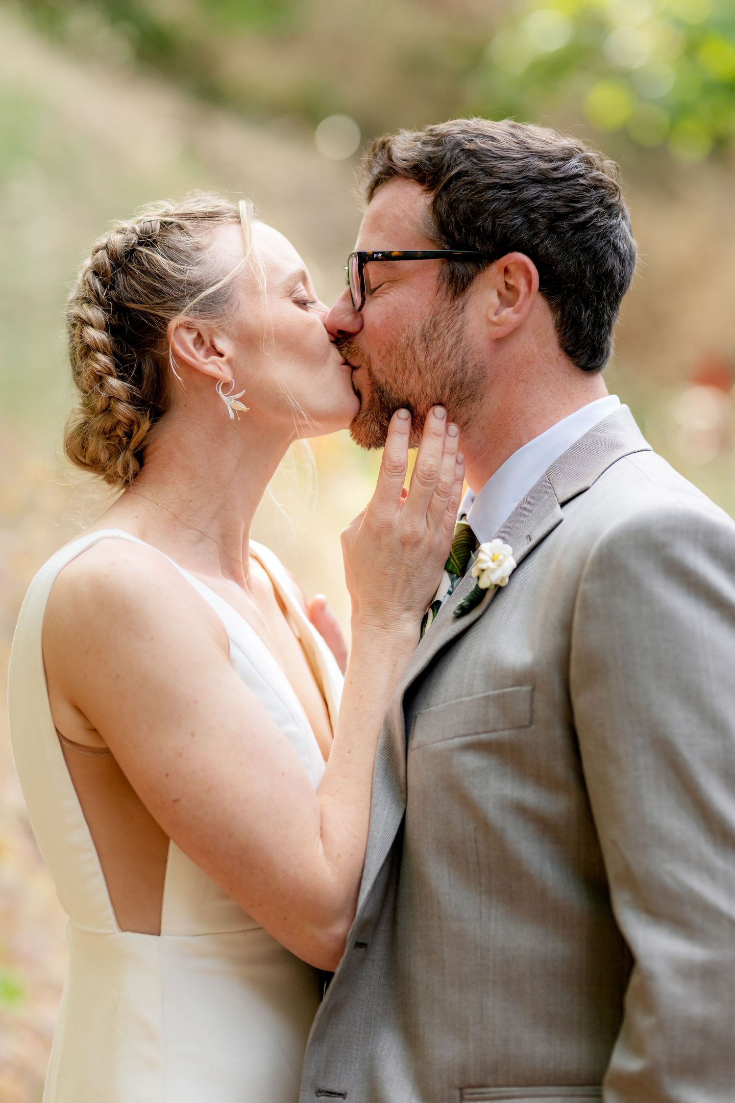Bride and groom share a romantic kiss outdoors in natural sunlight on their wedding day.