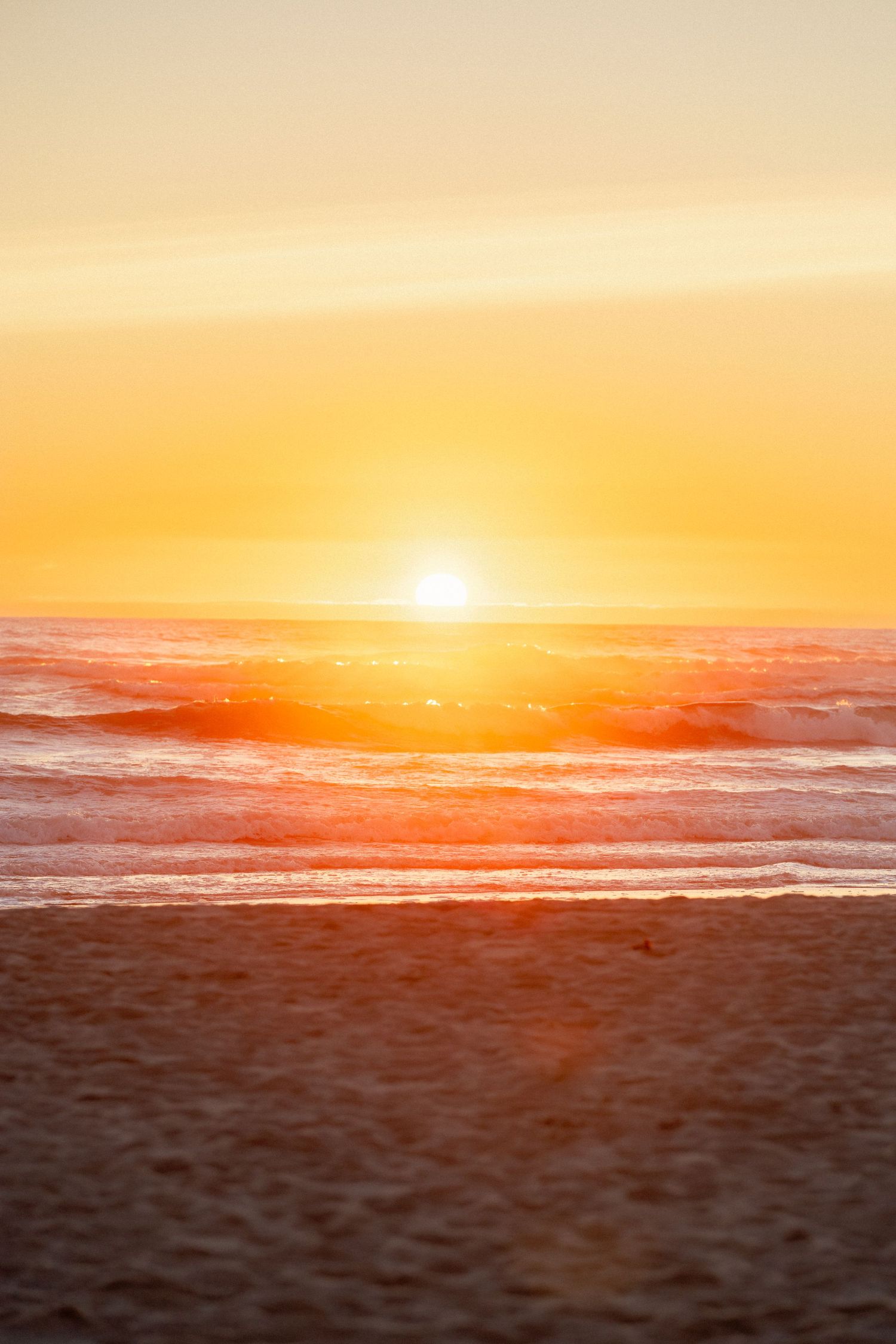 Golden sunset over ocean waves on sandy beach with vibrant orange sky reflecting on the water.