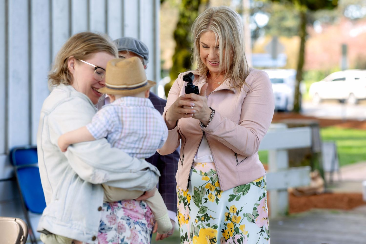 Two women looking at a smartphone while one holds a baby outdoors.