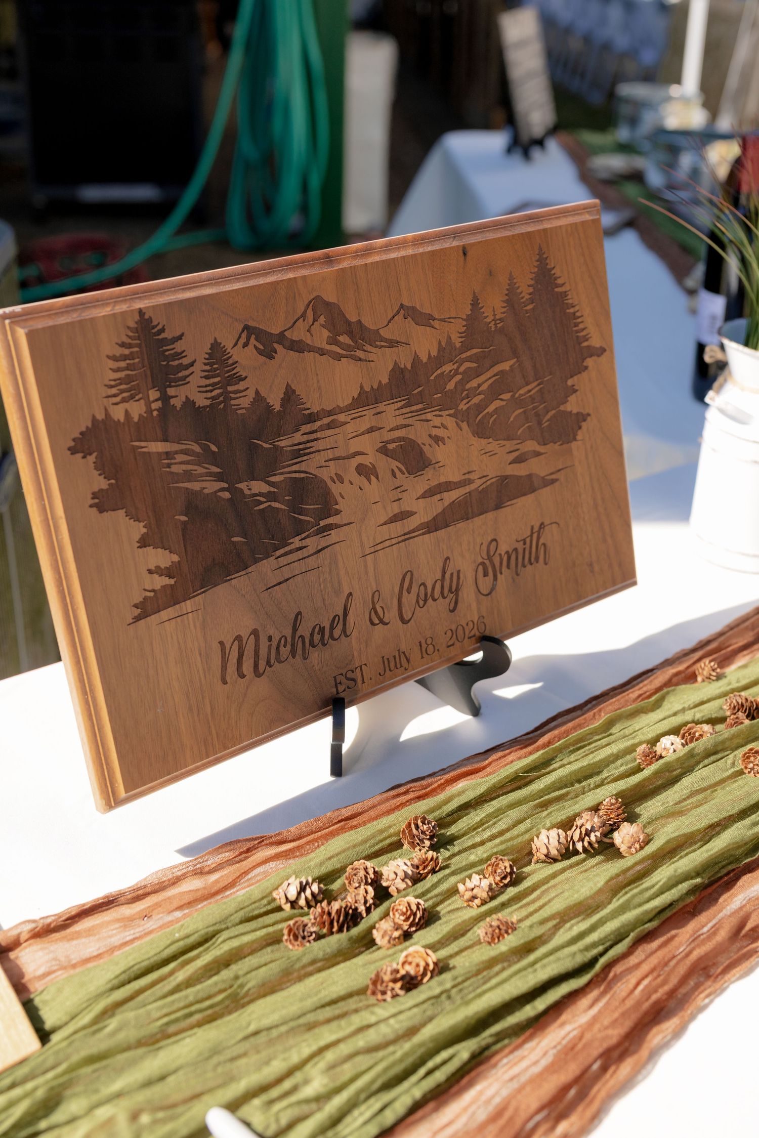 Personalized engraved wooden wedding cutting board for Michael & Cody Smith with mountain landscape design and pine cones.