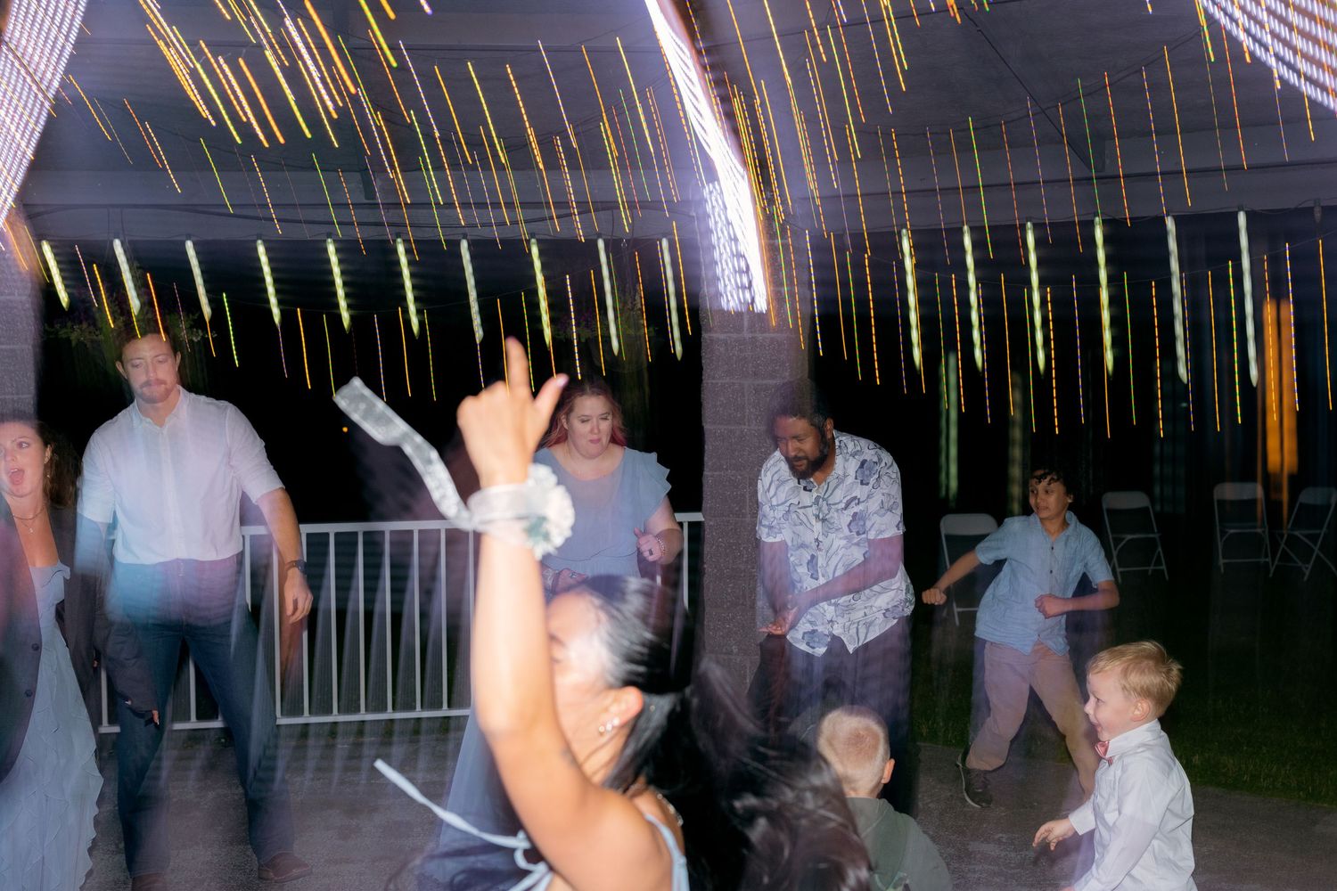 Guests dancing and celebrating at an outdoor wedding reception with colorful streamers and string lights.