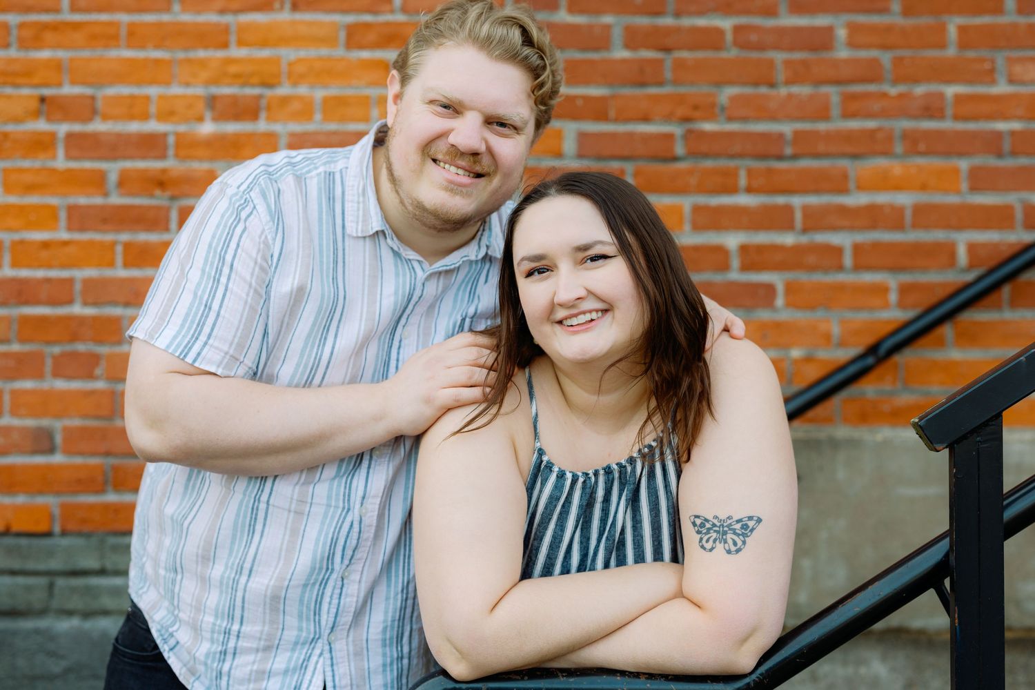 Couple sharing a laugh while sitting together on outdoor steps with red brick wall background.