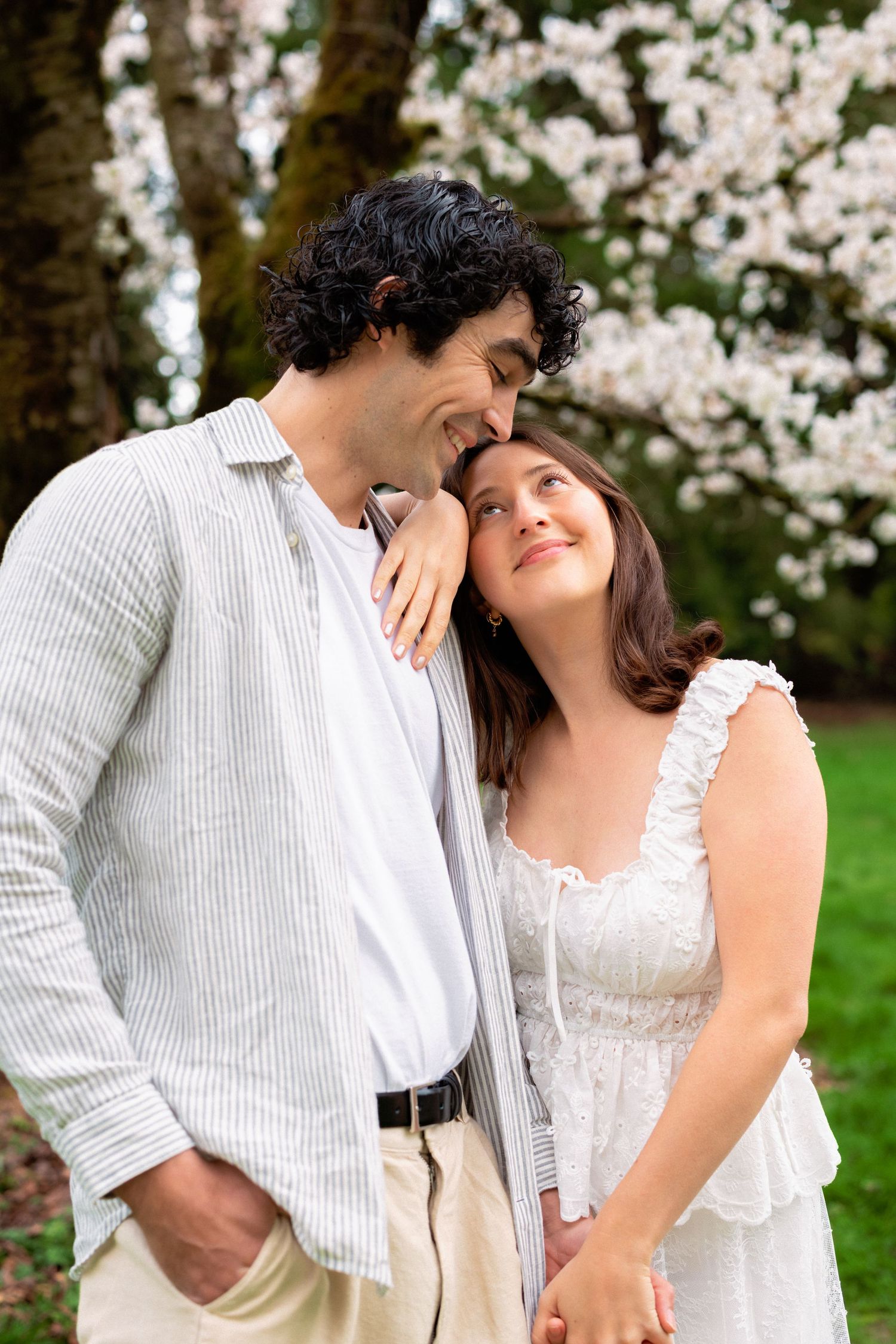 A romantic moment shared between a couple beneath flowering cherry blossom trees in a park.