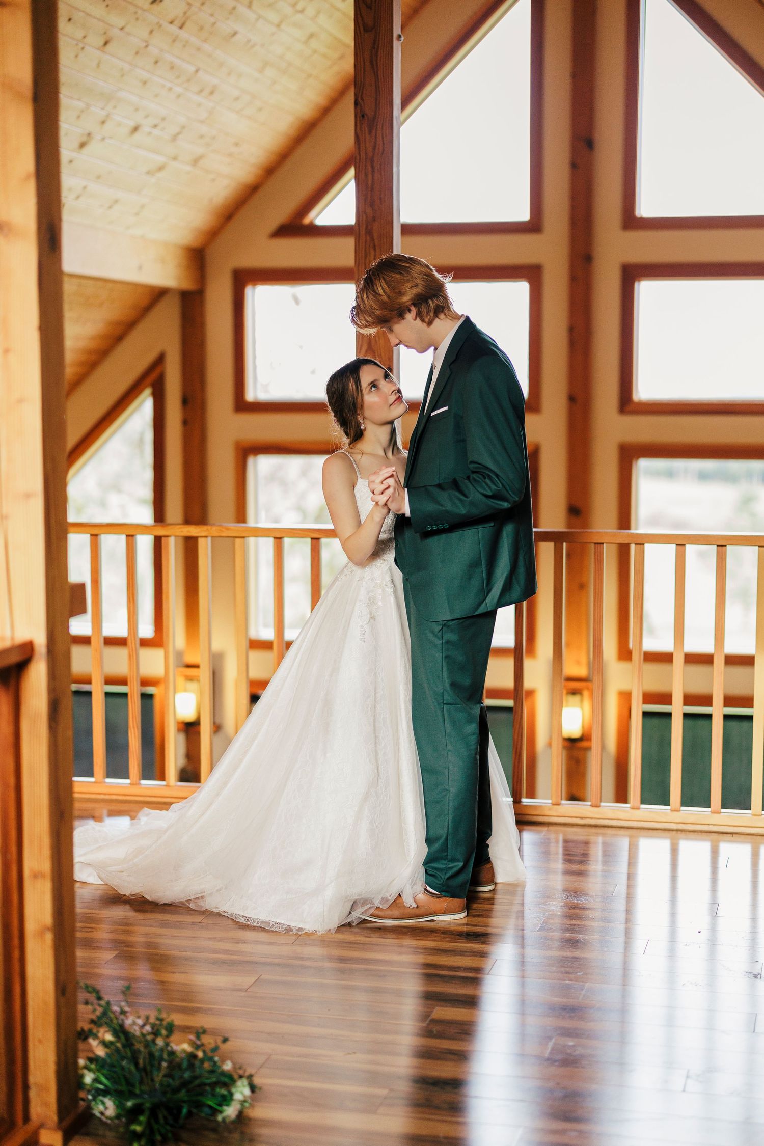 A couple in wedding attire share an intimate moment in a rustic wooden lodge with vaulted ceilings and natural lighting.