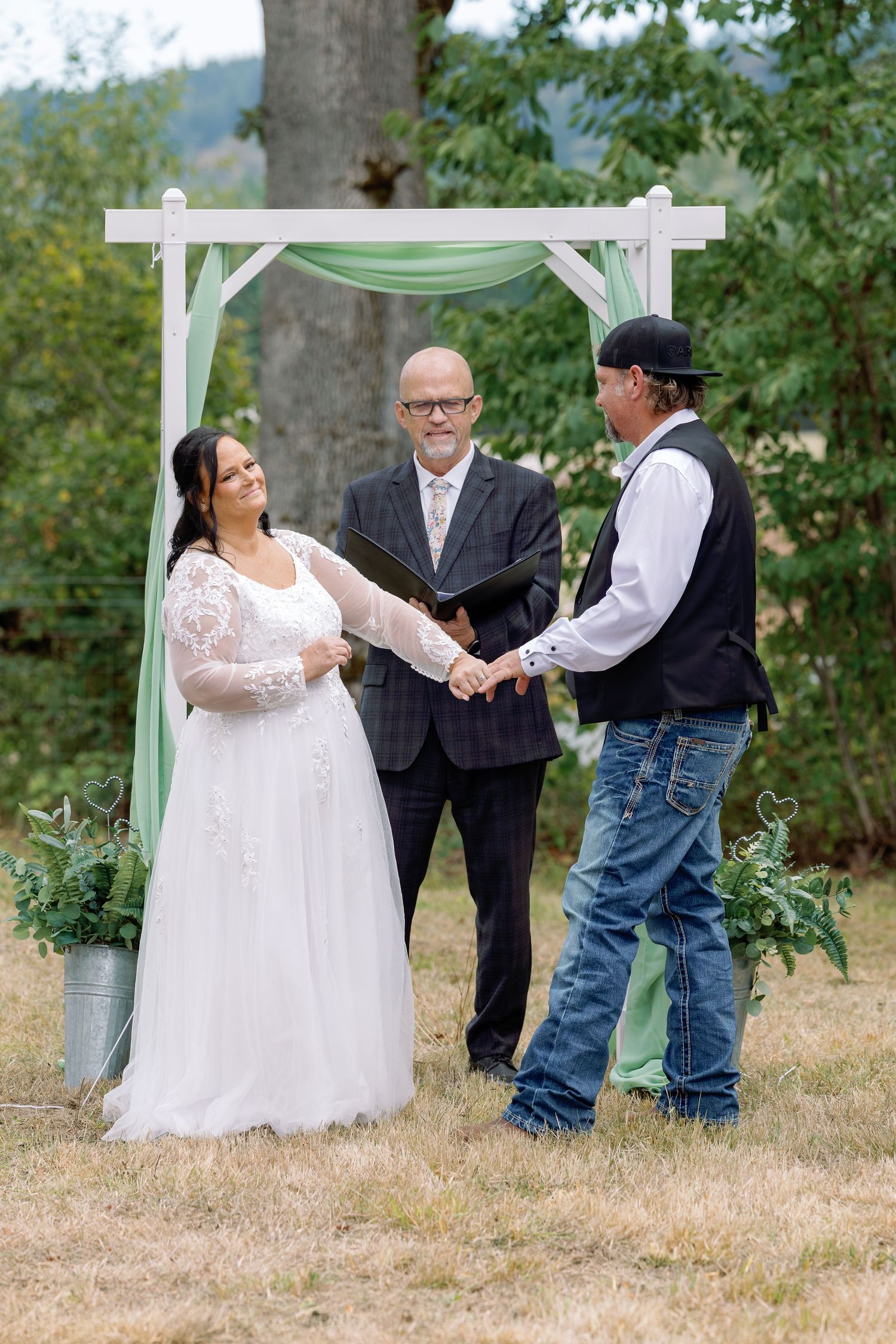 A joyful wedding celebration unfolds beneath a white pergola in a natural outdoor setting.