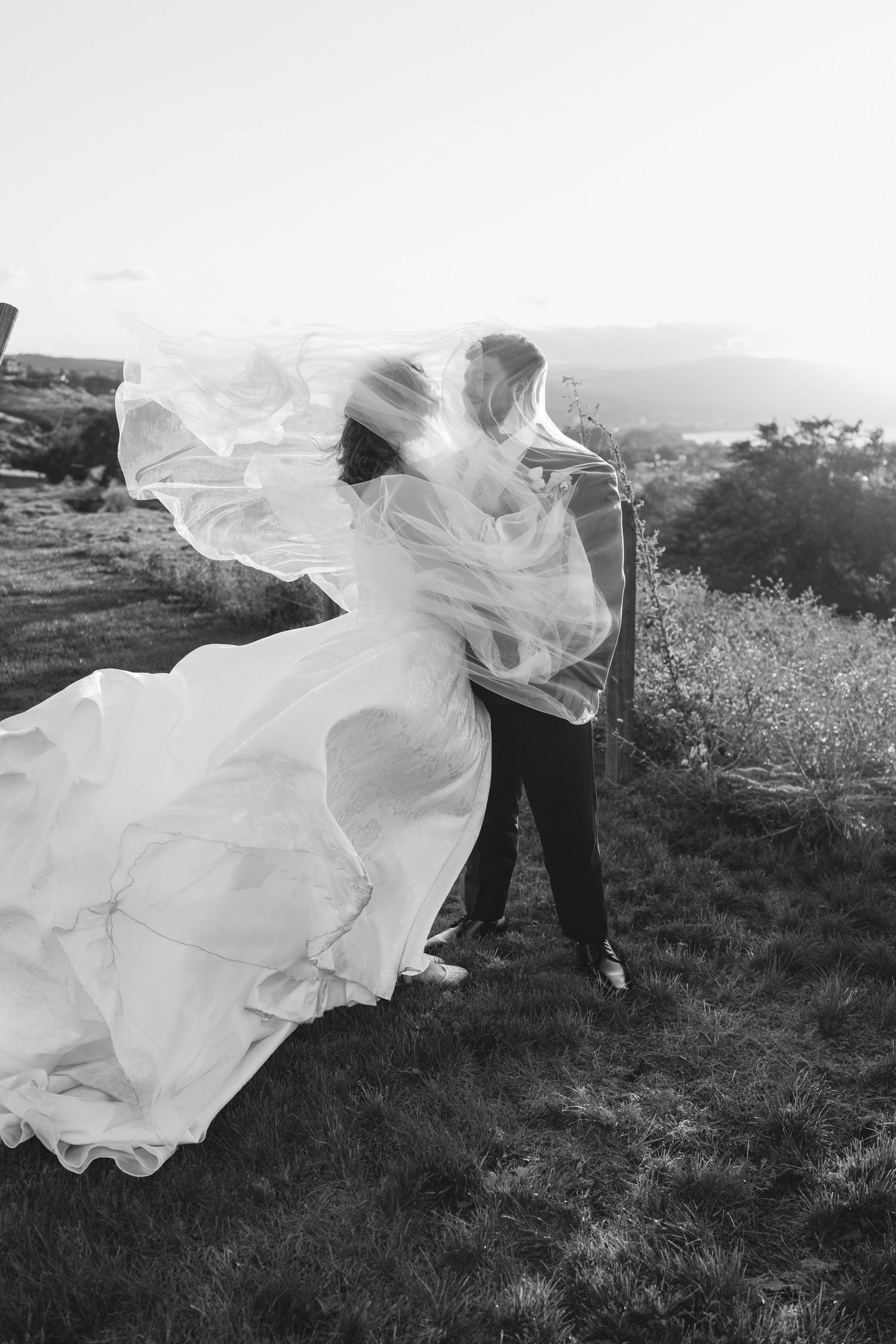 A flowing white wedding dress billows dramatically in the wind during an outdoor photoshoot.