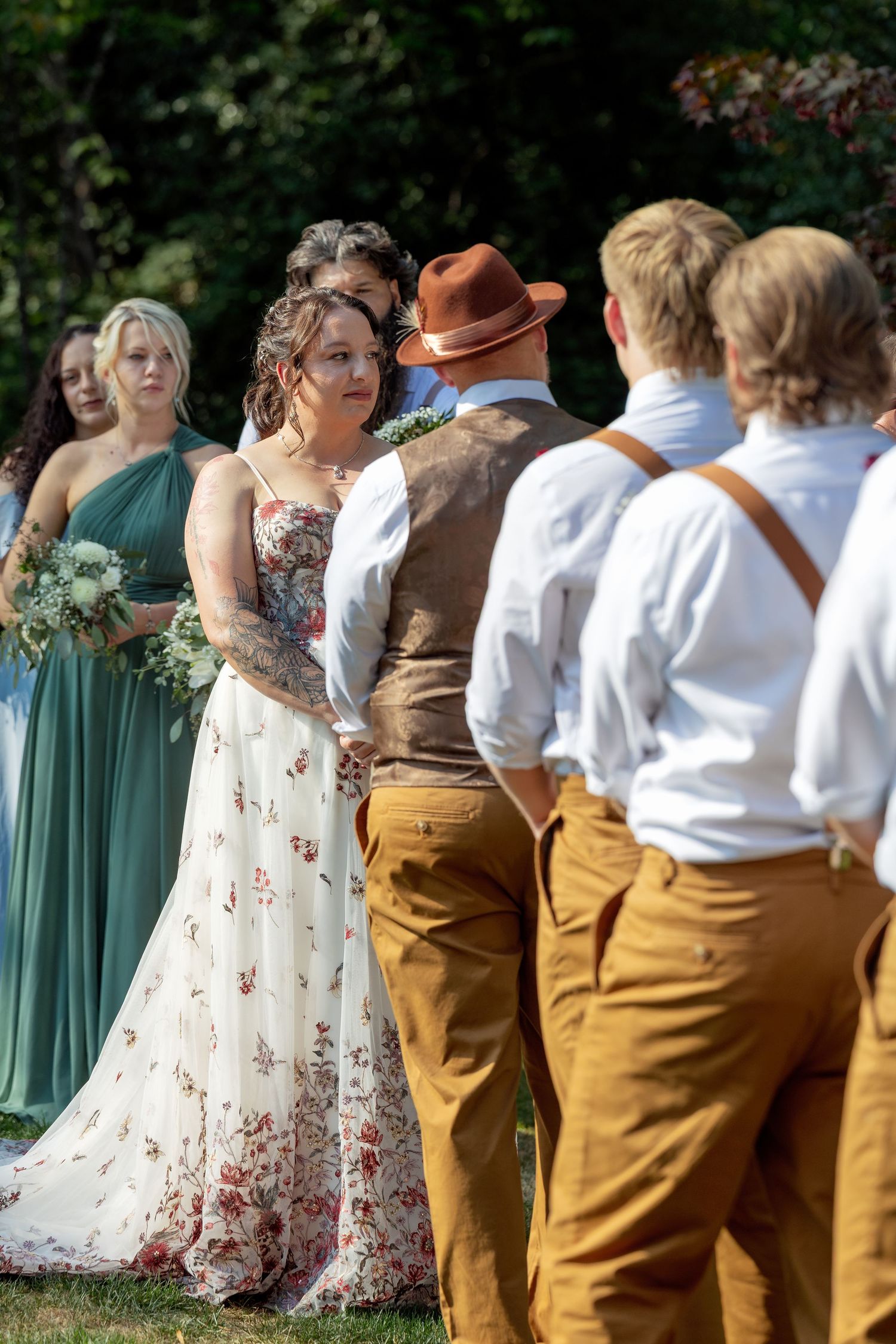 Wedding party lined up outdoors wearing sage green dresses and mustard yellow pants with white shirts.