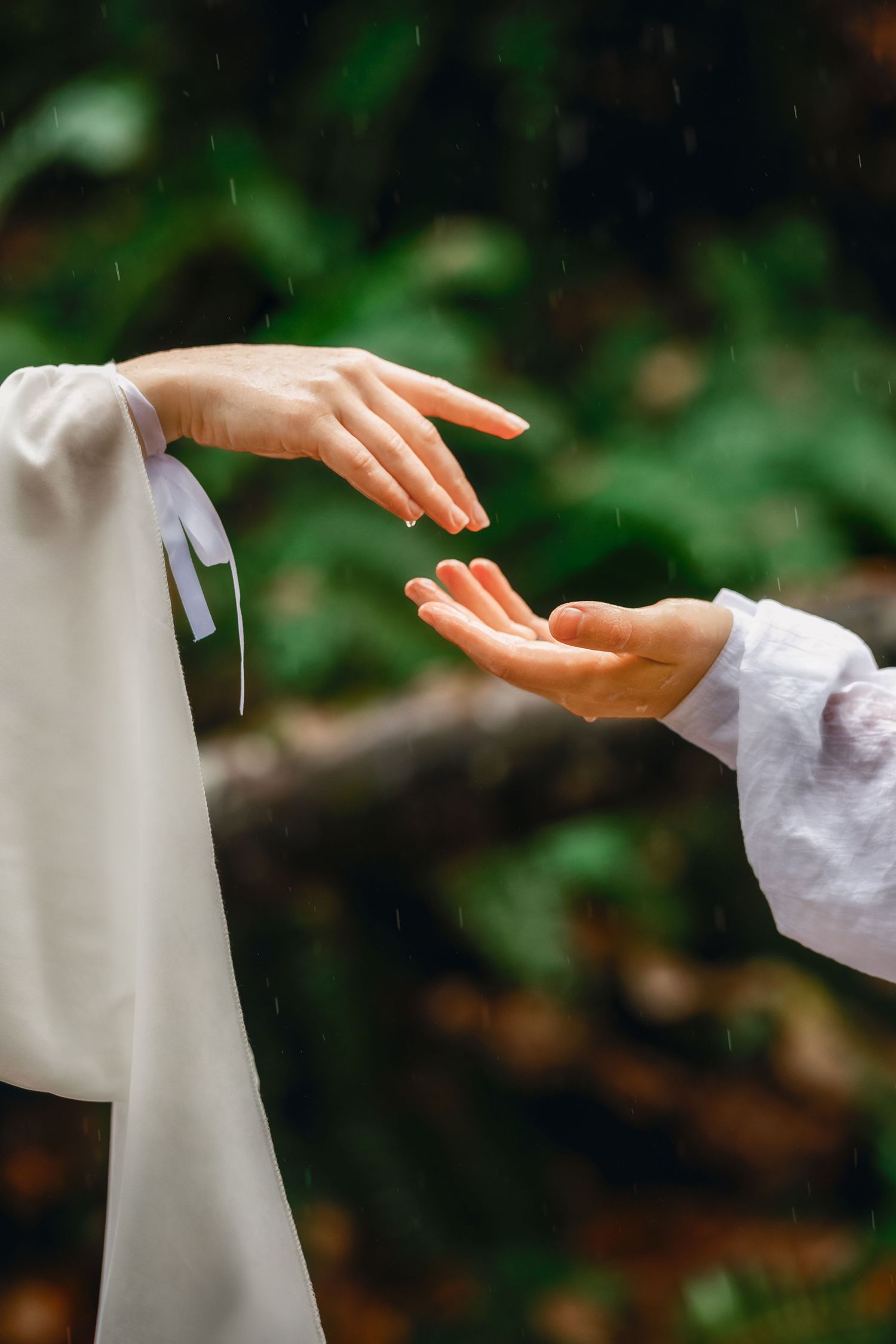 Close-up of hands reaching towards each other against a blurred natural background.