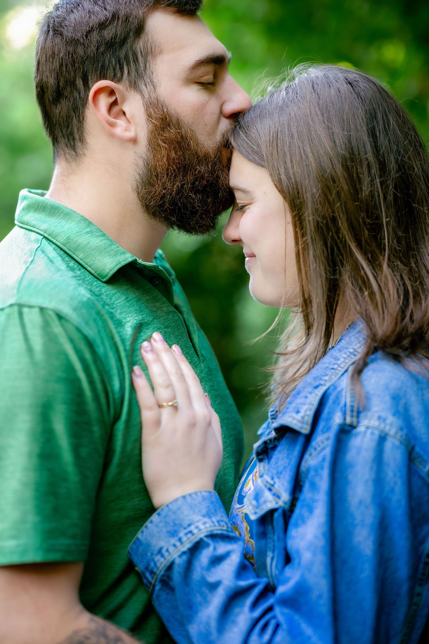 A romantic couple in green and denim share tender moments against a blurred natural backdrop.