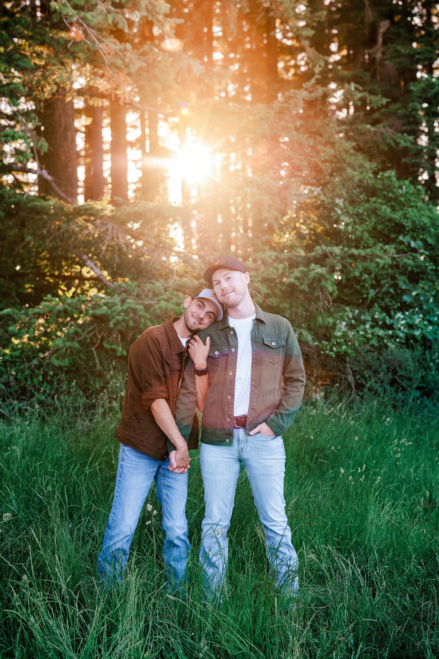 Three people standing together in a grassy field at sunset with warm lighting.