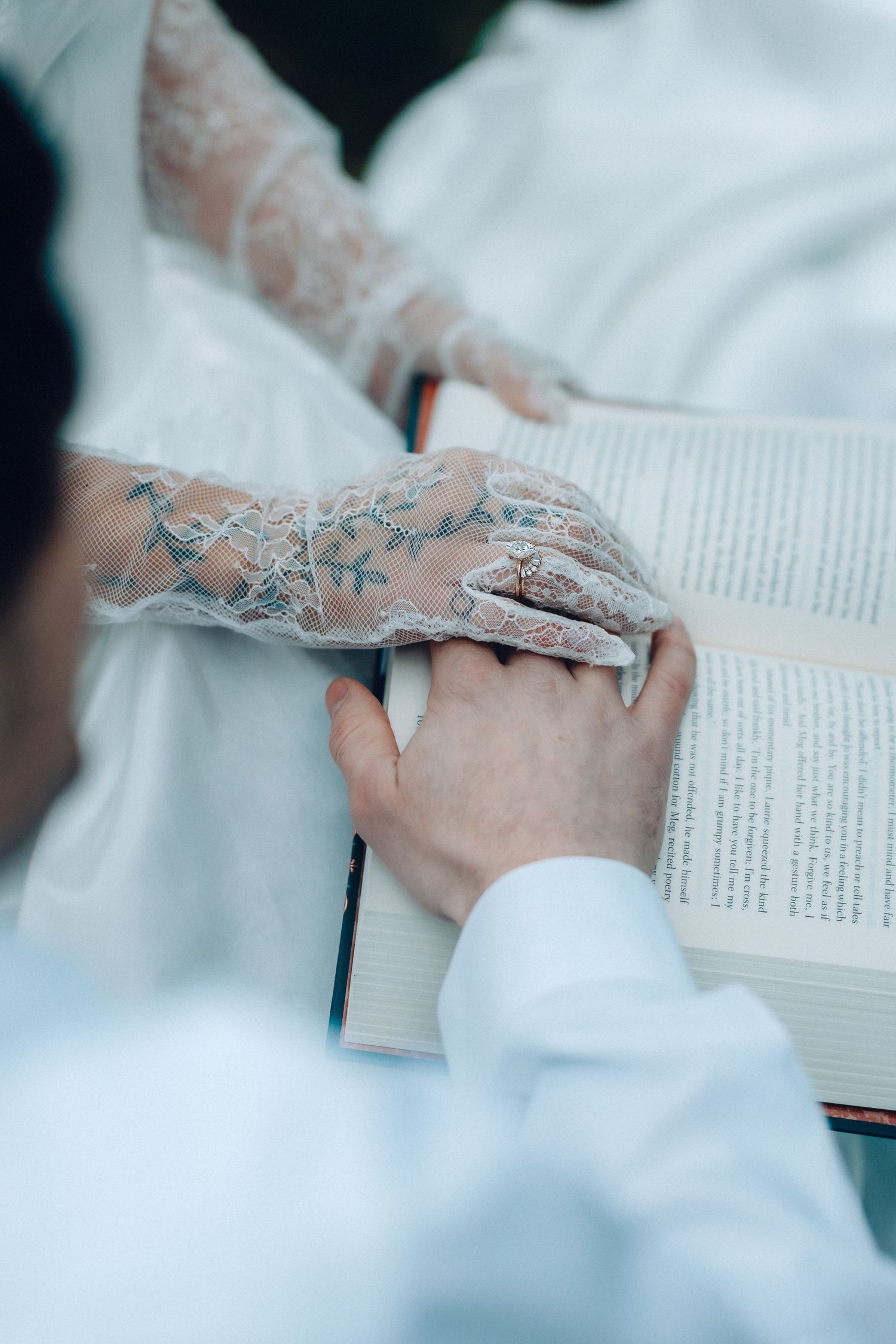 A close-up view of hands in white lace sleeves holding open a book with text pages.
