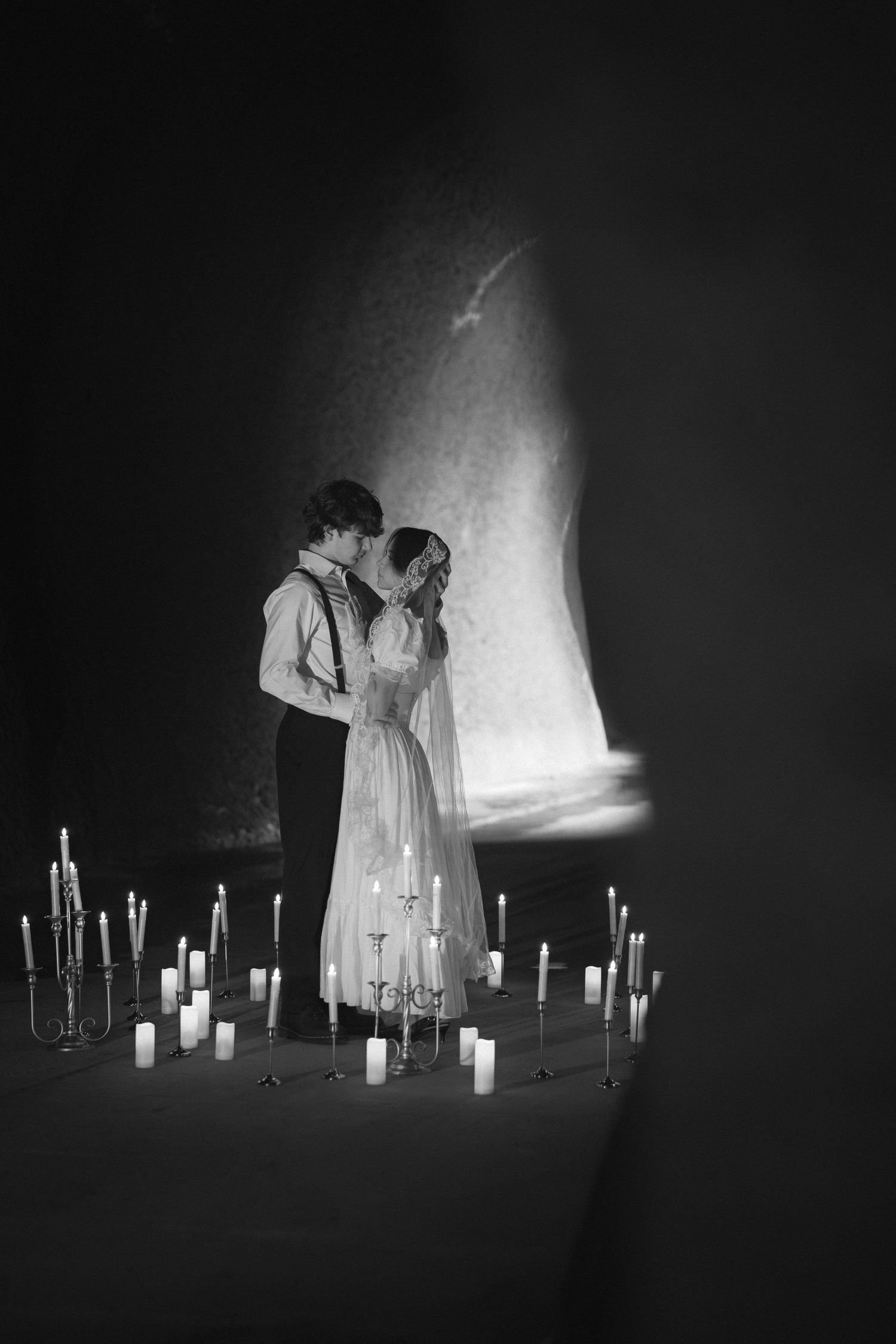 A figure in white stands among glowing candles in a dark room creating an ethereal atmospheric scene.