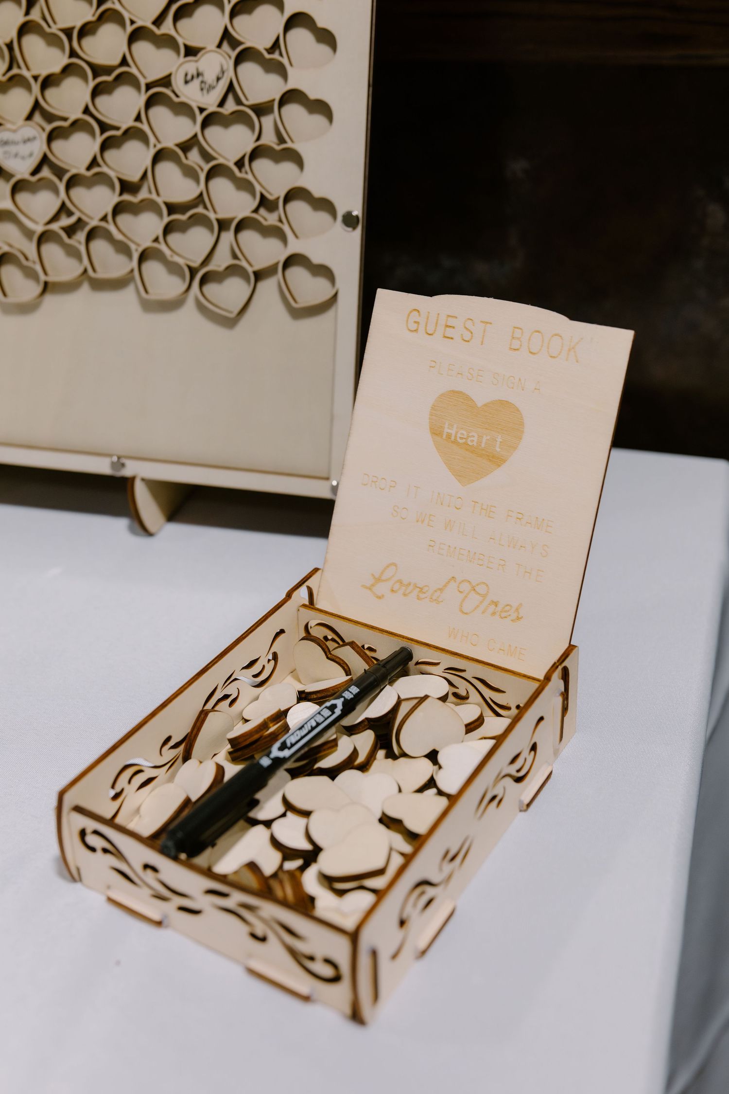 Wooden laser-cut wedding guest book box with heart-shaped tiles and a marker for signing.