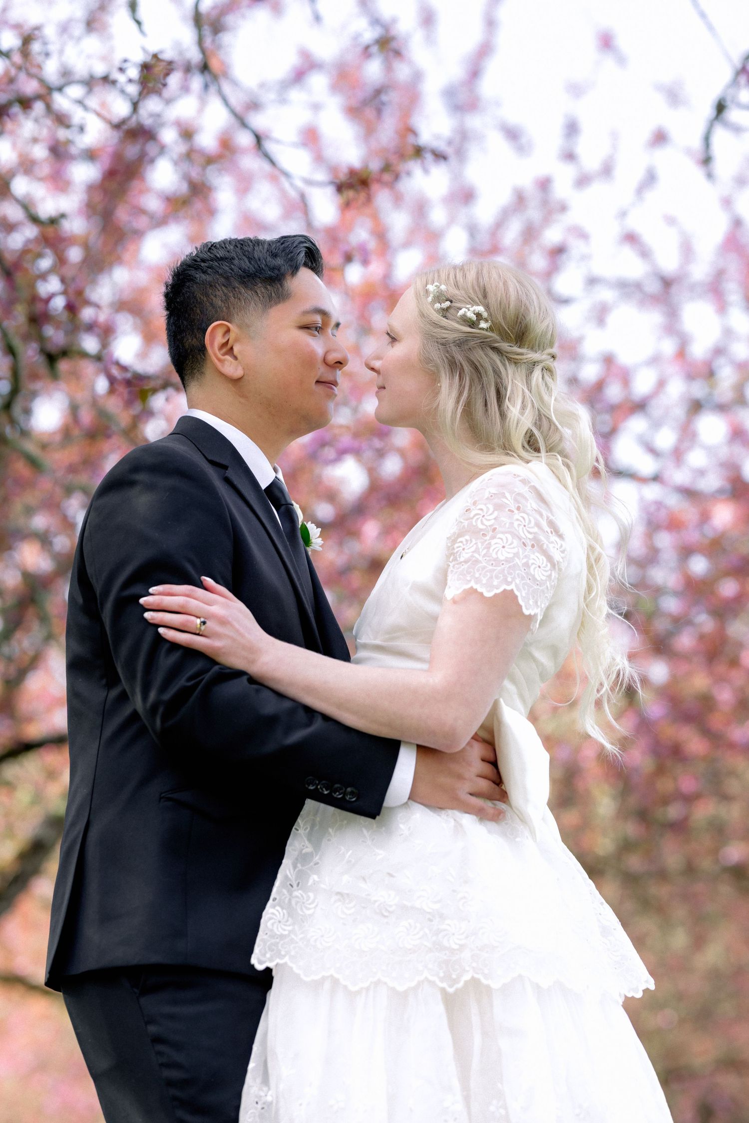 Bride and groom share a romantic moment outdoors surrounded by pink cherry blossoms in a spring wedding portrait.