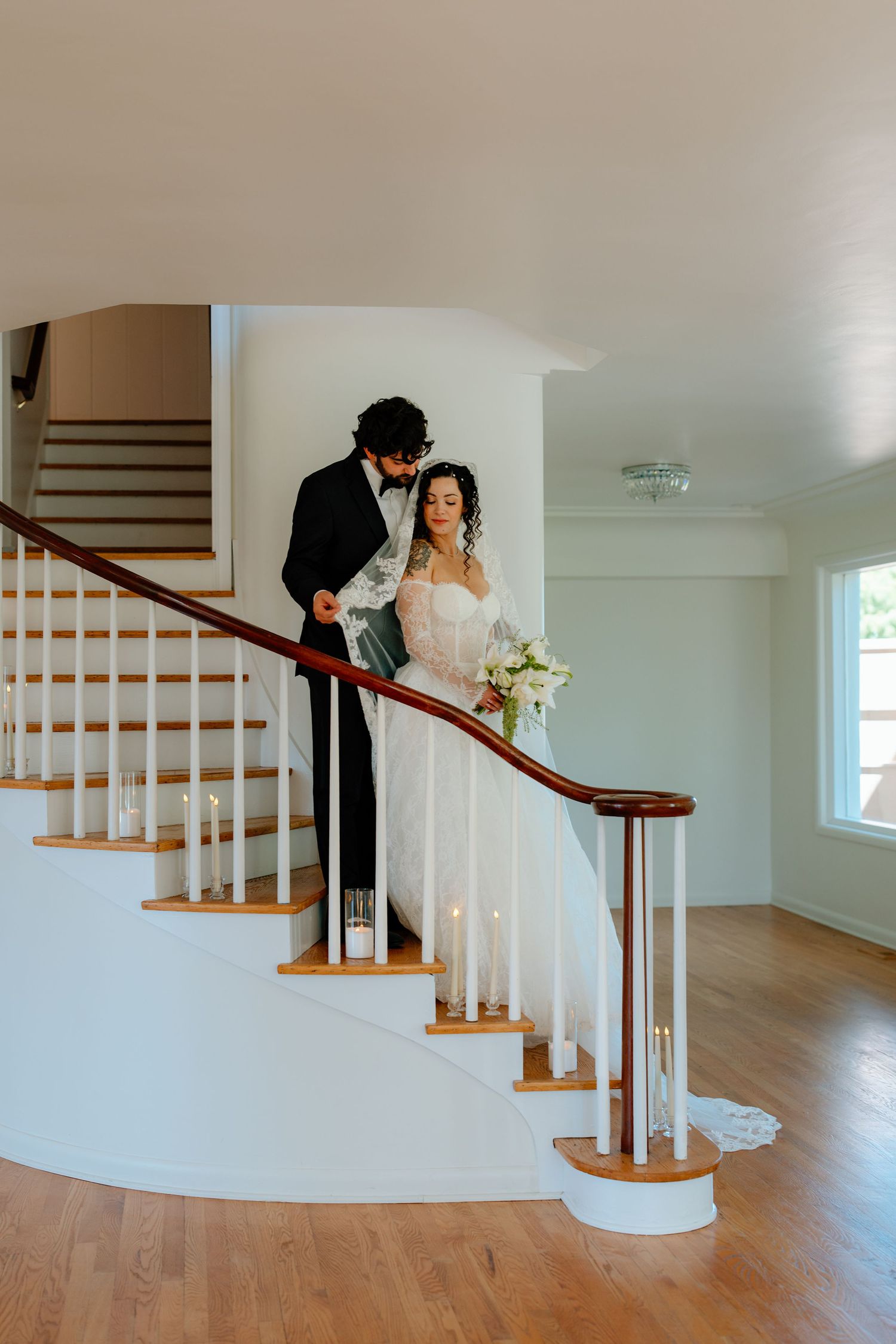 Bride and groom share an intimate moment on an elegant curved staircase, bride holding white floral bouquet.