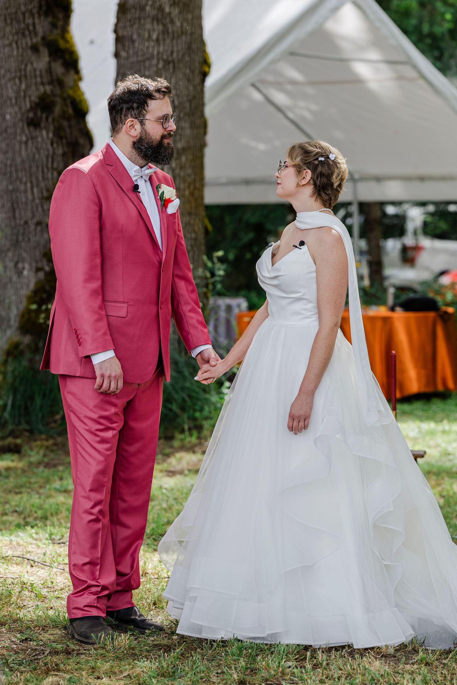 A couple shares a sweet moment at their outdoor wedding, with the groom in a pink suit and bride in a white ballgown.