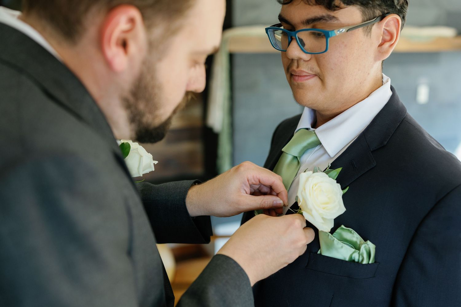 Close-up shots of boutonniere and tie adjustments during wedding preparations.