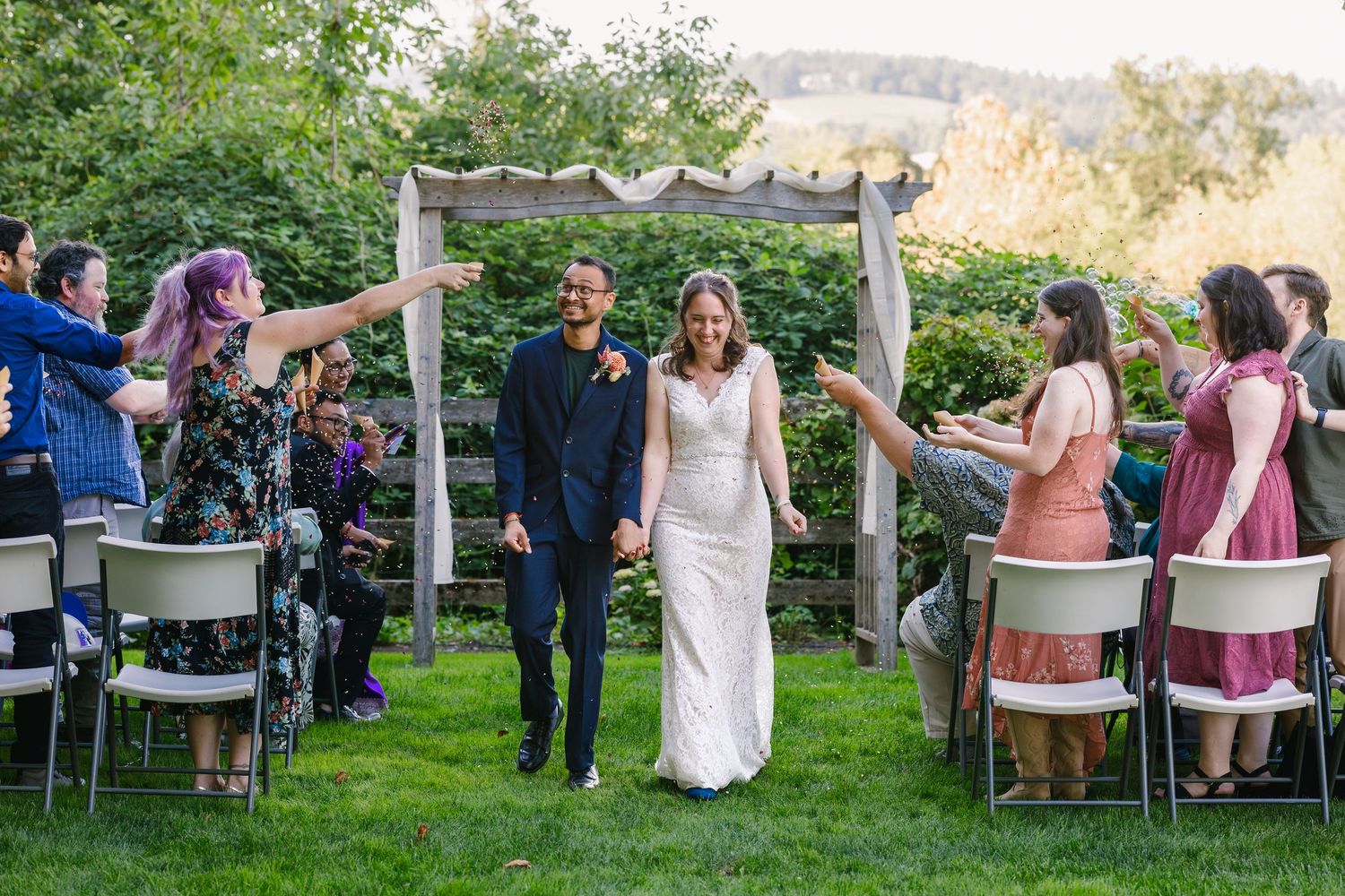 Outdoor wedding reception with guests seated at tables under trees.