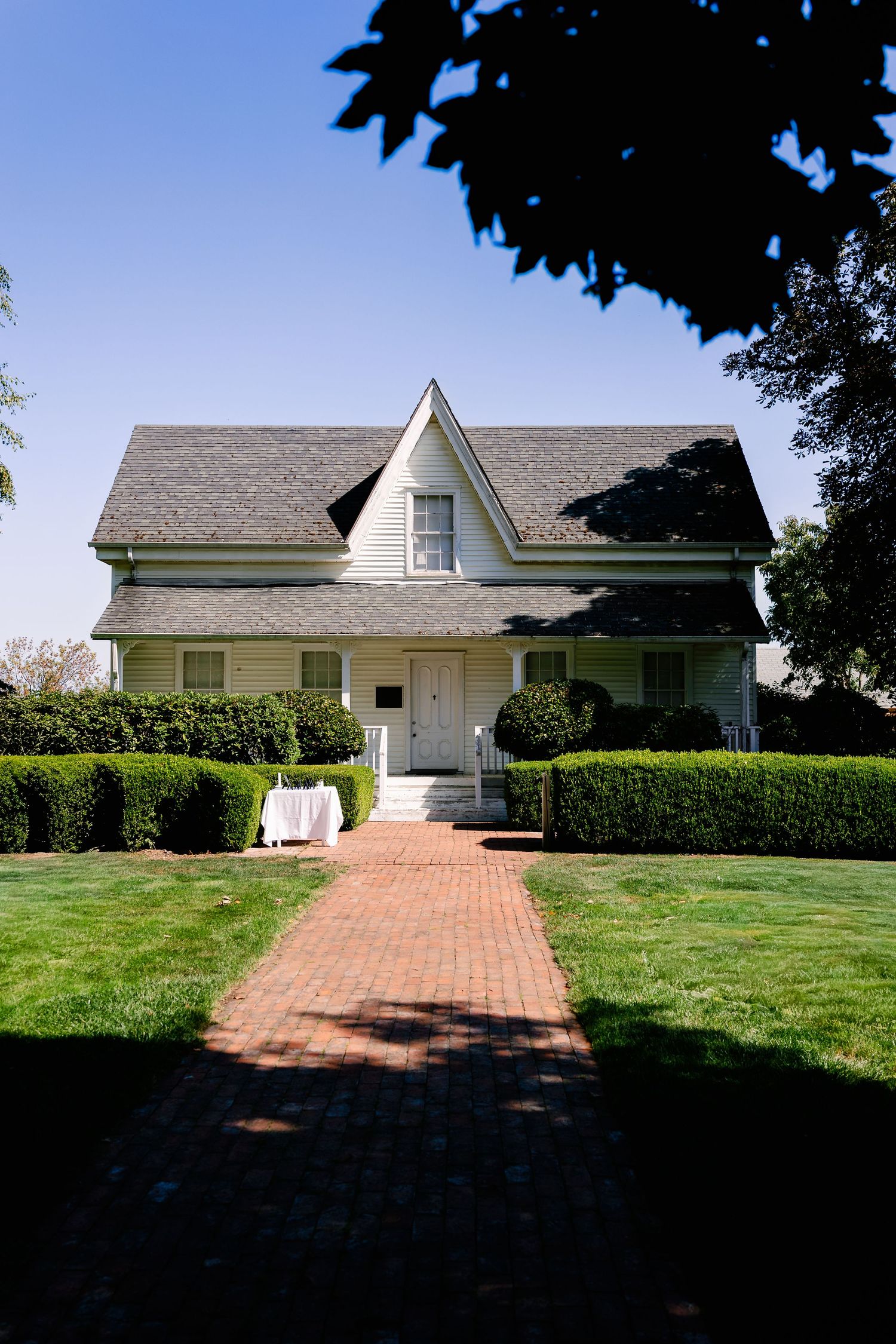 White farmhouse style home with brick pathway and manicured lawn in daylight.