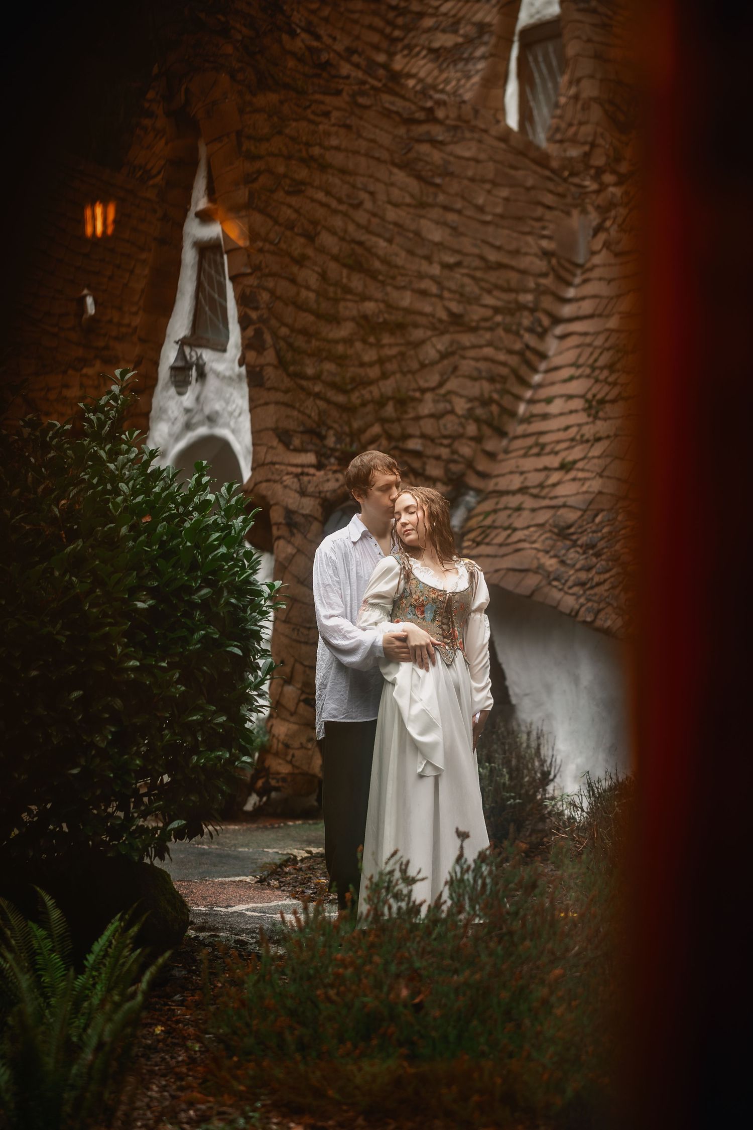 Figures in flowing white garments pose against textured stone walls in a mystical garden setting.