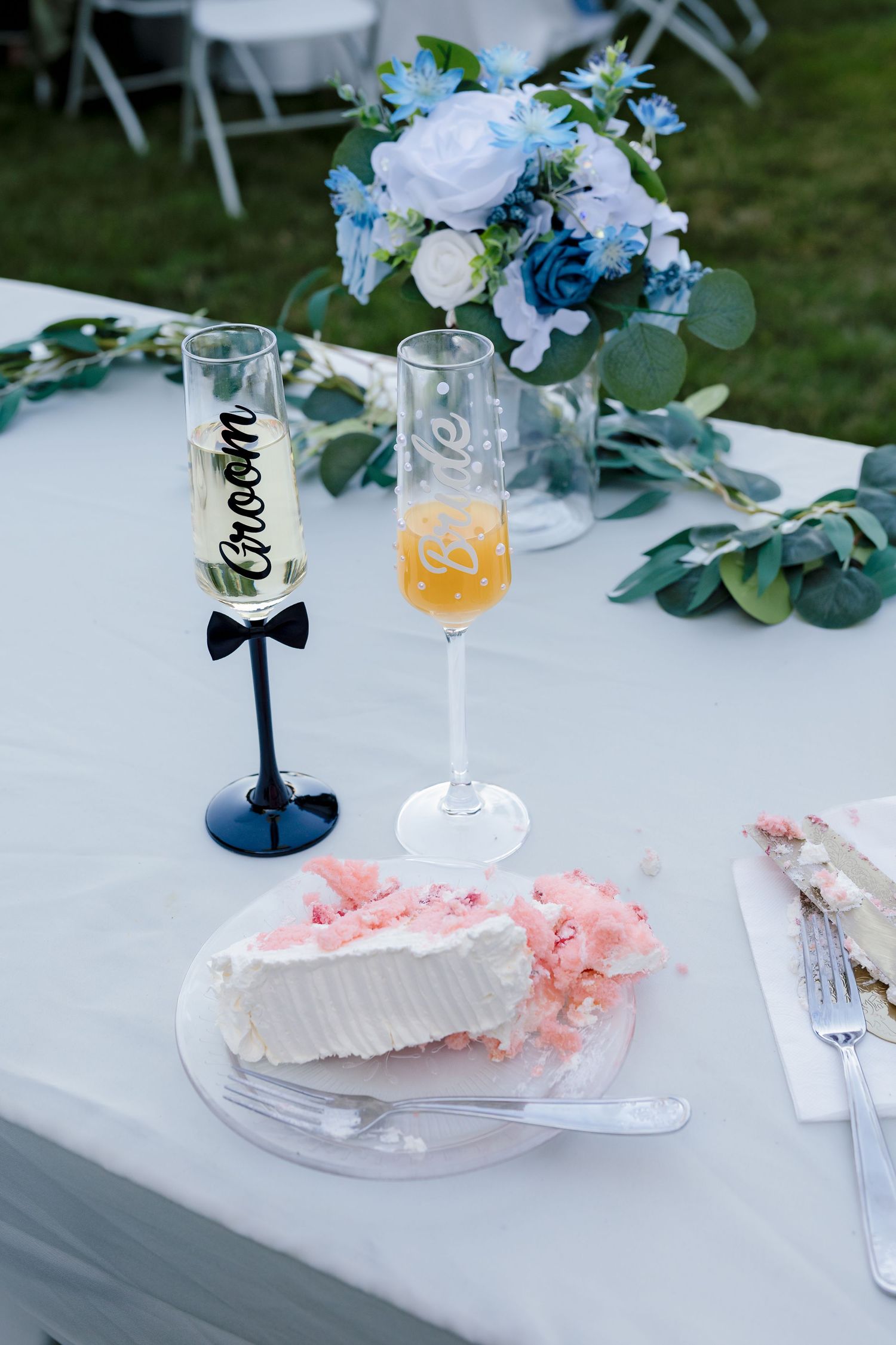 Wedding sweetheart table with cake slice, Bride and Groom champagne flutes, and blue floral centerpiece.