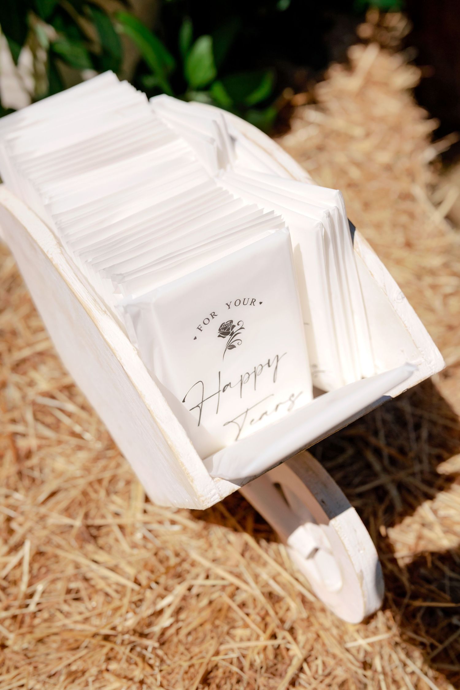White wheelbarrow filled with Happy Tears tissue packets as wedding ceremony favors on hay bales.