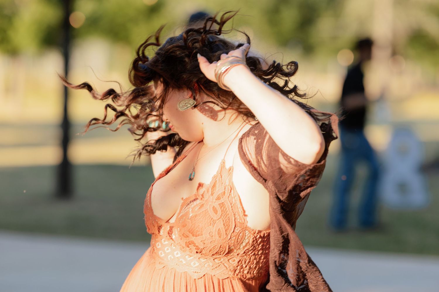 Woman in elegant peach lace dress with curly hair blowing in the wind at an outdoor wedding reception.